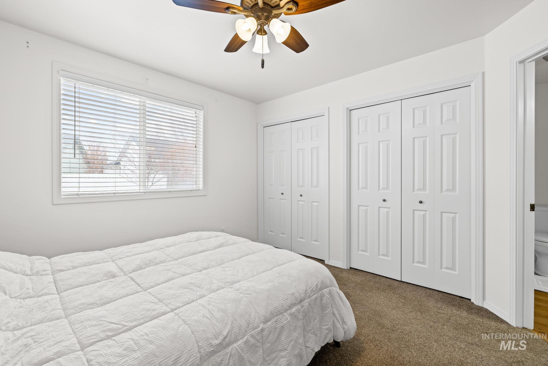 Bedroom featuring multiple closets, dark colored carpet, and a ceiling fan