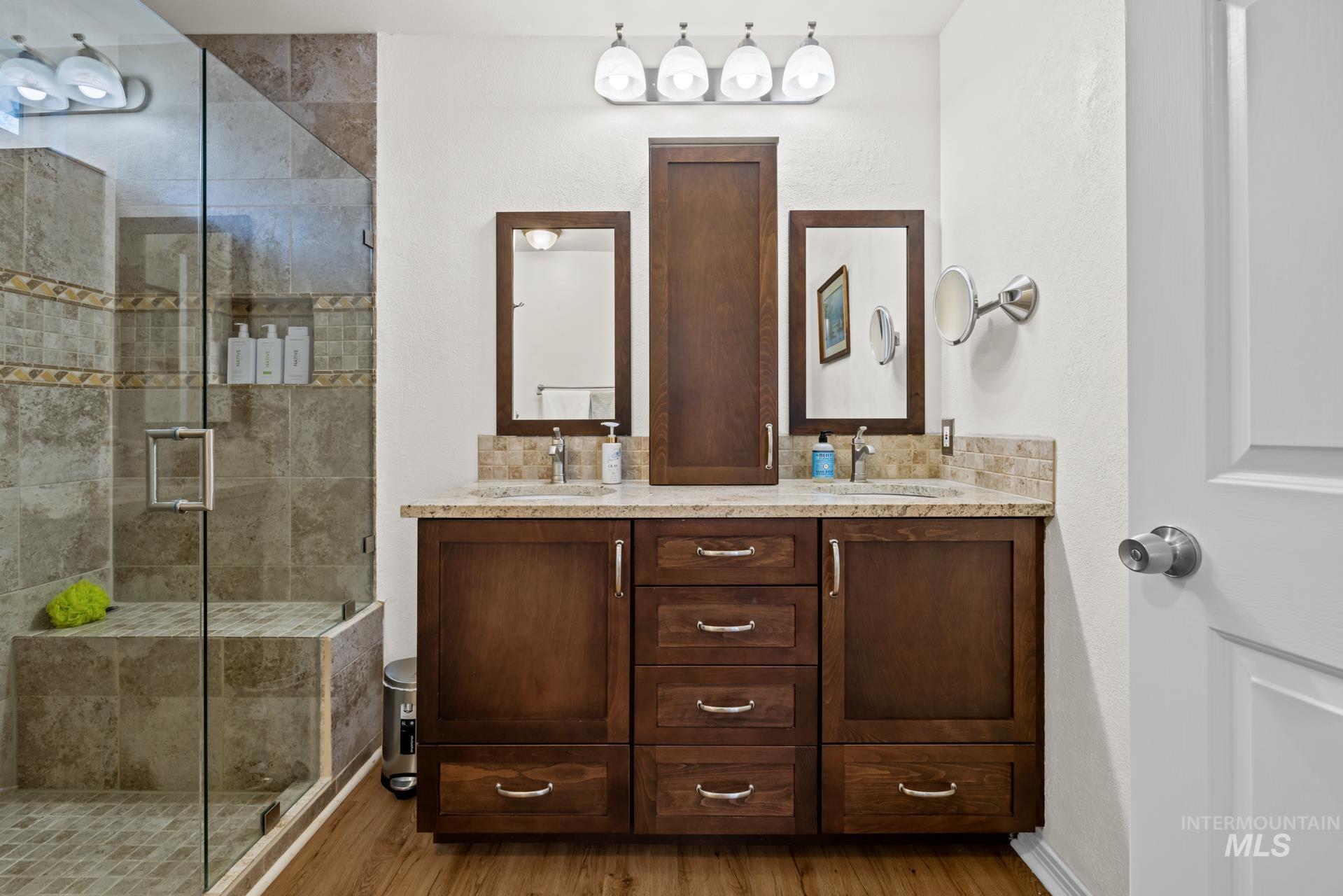 Full bath featuring double vanity, a shower stall, and light wood-type flooring