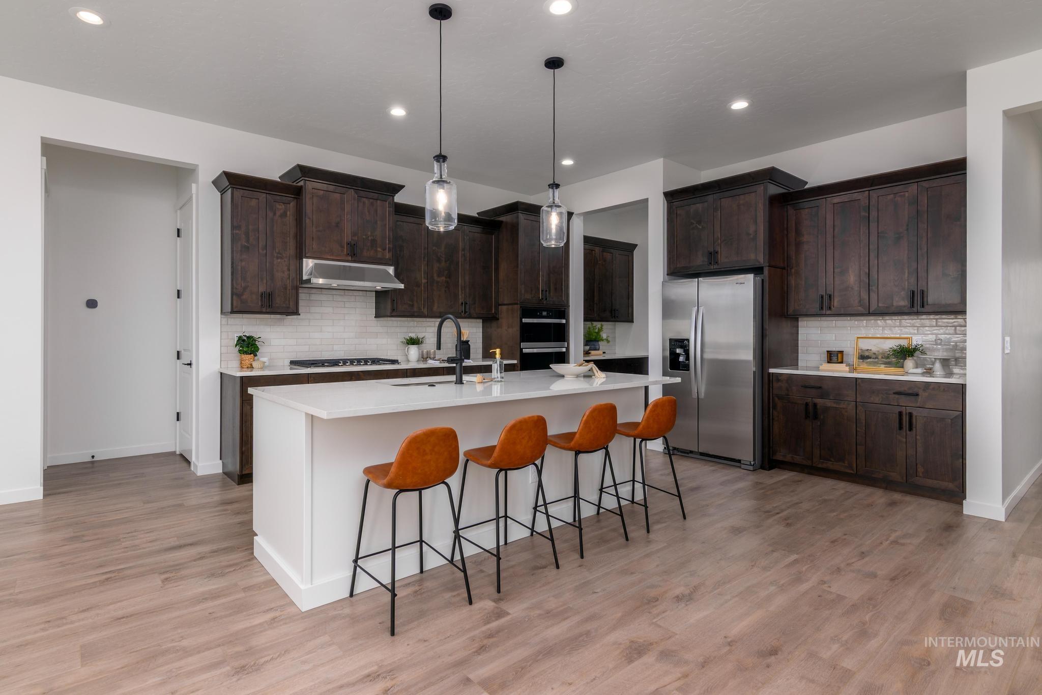 Kitchen featuring pendant lighting, a breakfast bar area, appliances with stainless steel finishes, tasteful backsplash, and dark brown cabinetry