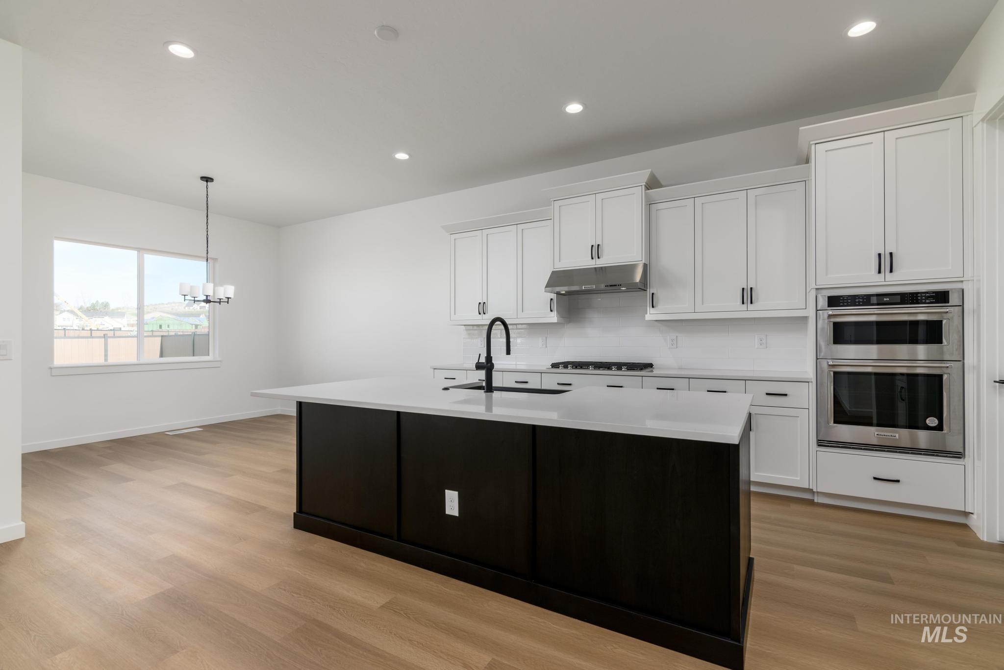 Kitchen with white cabinetry, recessed lighting, an island with sink, decorative light fixtures, and light wood-type flooring