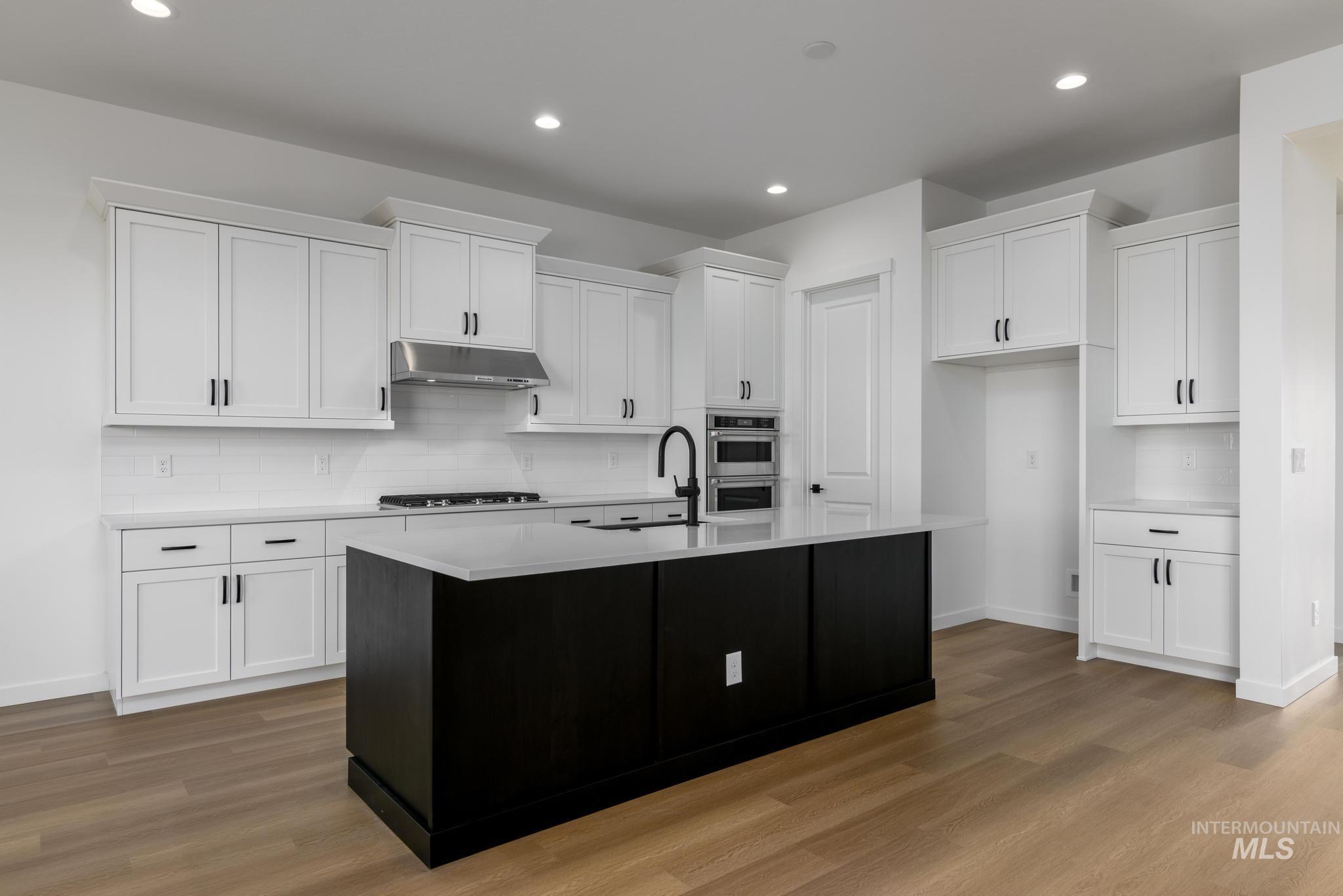 Kitchen with decorative backsplash, white cabinetry, light wood-style flooring, an island with sink, and recessed lighting