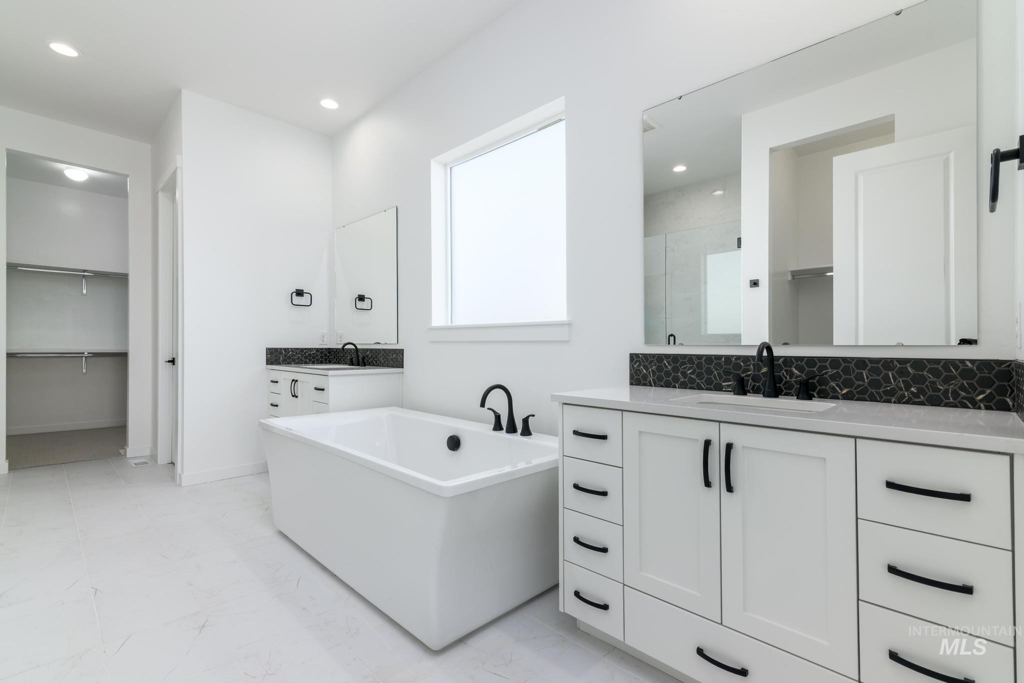 Bathroom featuring a walk in closet, two vanities, a freestanding bath, a shower stall, and recessed lighting