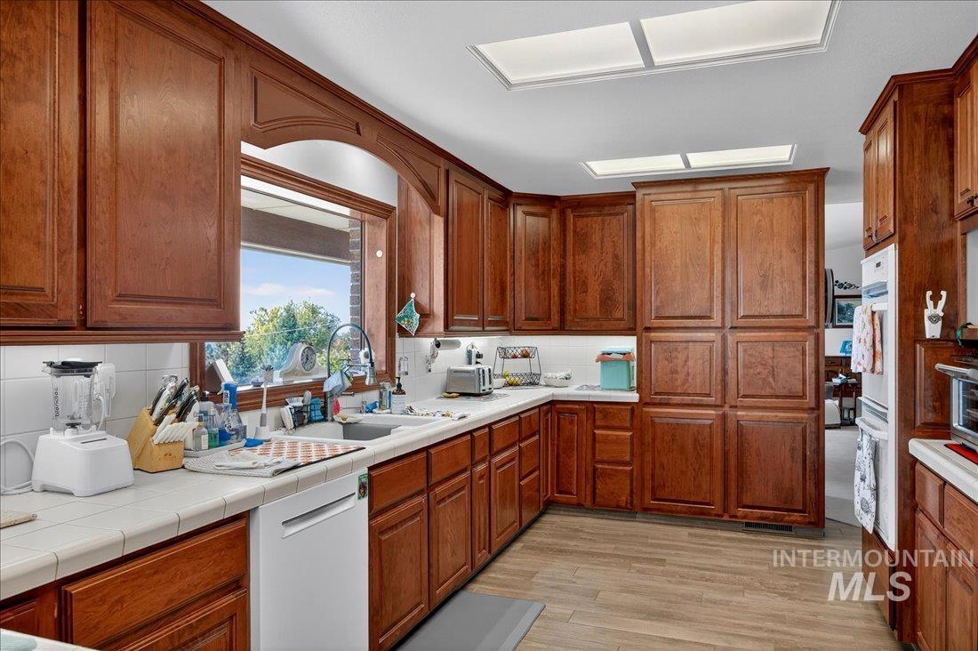 Kitchen with white appliances, light wood-style floors, brown cabinets, decorative backsplash, and tile countertops
