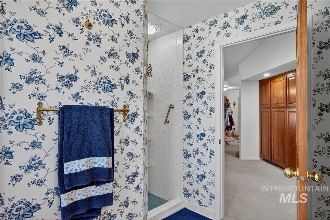 Full bath featuring a shower stall, wallpapered walls, and light colored carpet