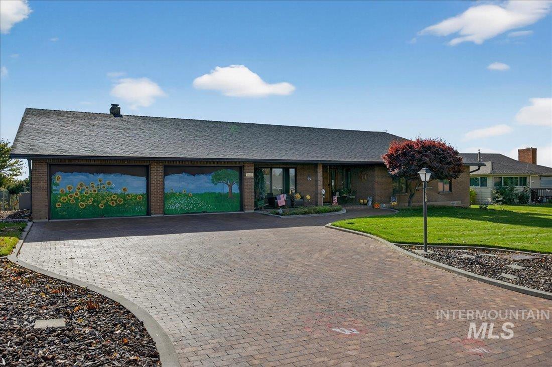 Ranch-style home with a front lawn, an attached garage, decorative driveway, brick siding, and a chimney