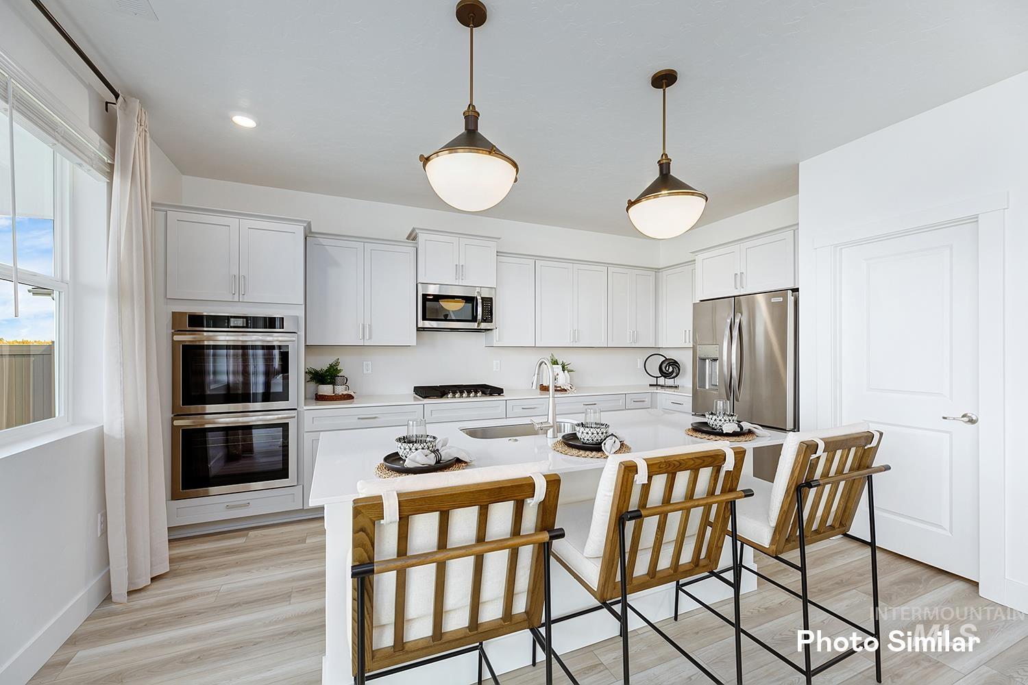 Kitchen with light wood-type flooring, stainless steel appliances, a breakfast bar, hanging light fixtures, and a center island with sink