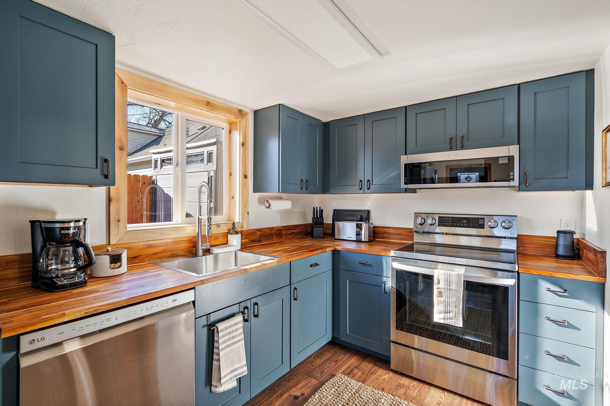 Kitchen featuring wooden counters, appliances with stainless steel finishes, dark wood finished floors, and blue cabinetry