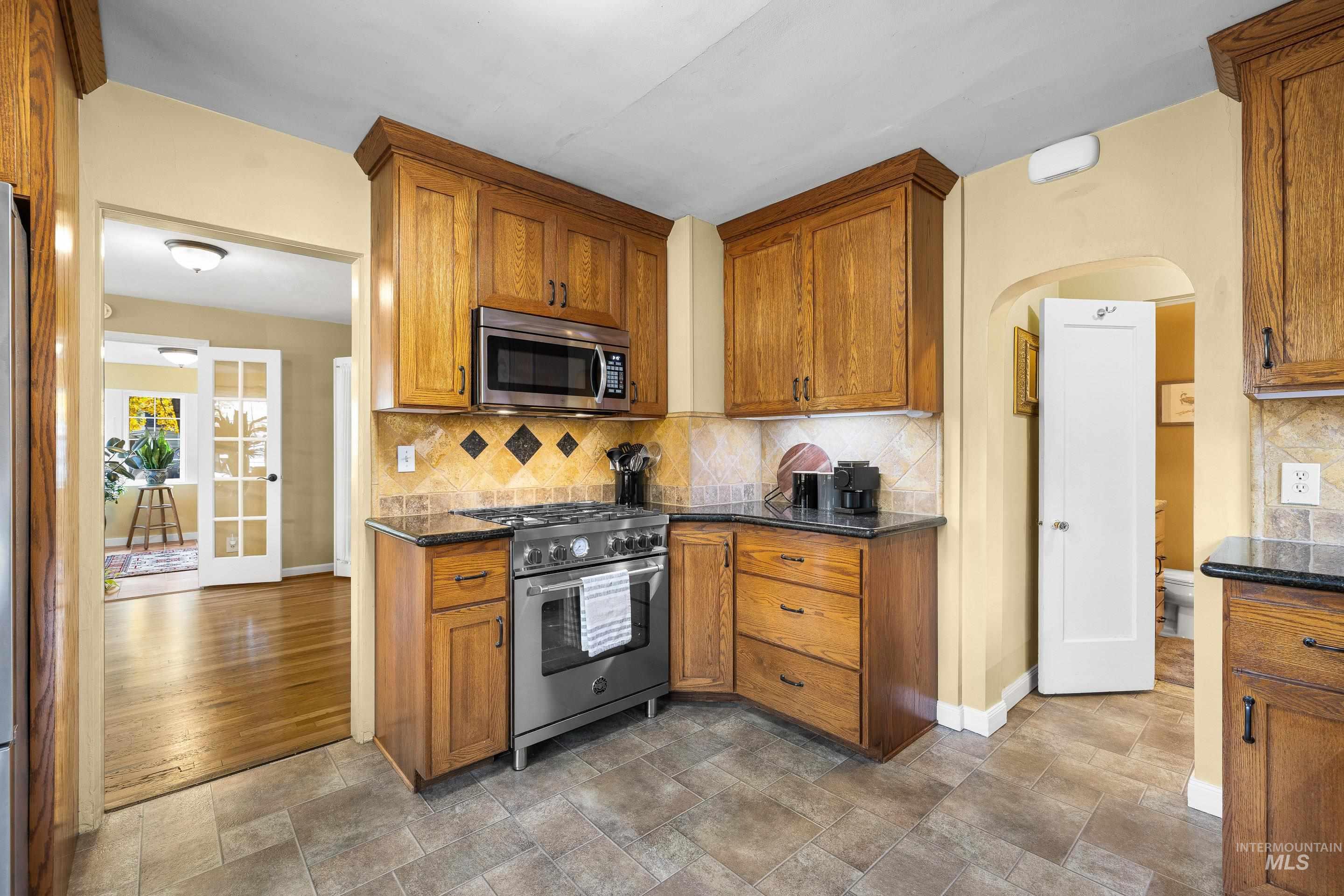 Kitchen featuring decorative backsplash, appliances with stainless steel finishes, arched walkways, stone finish floors, and brown cabinetry