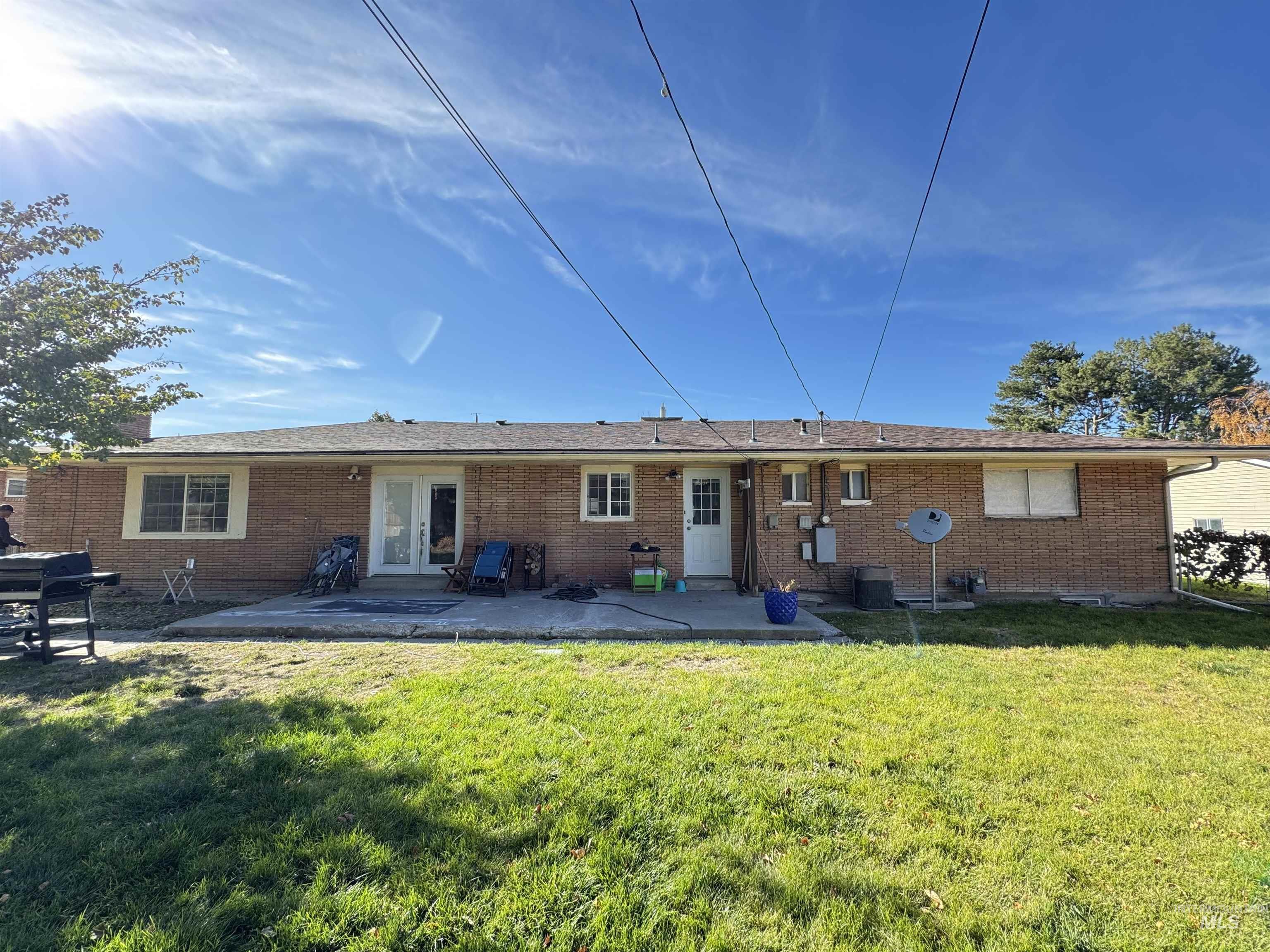 Back of property featuring brick siding, a lawn, and a patio