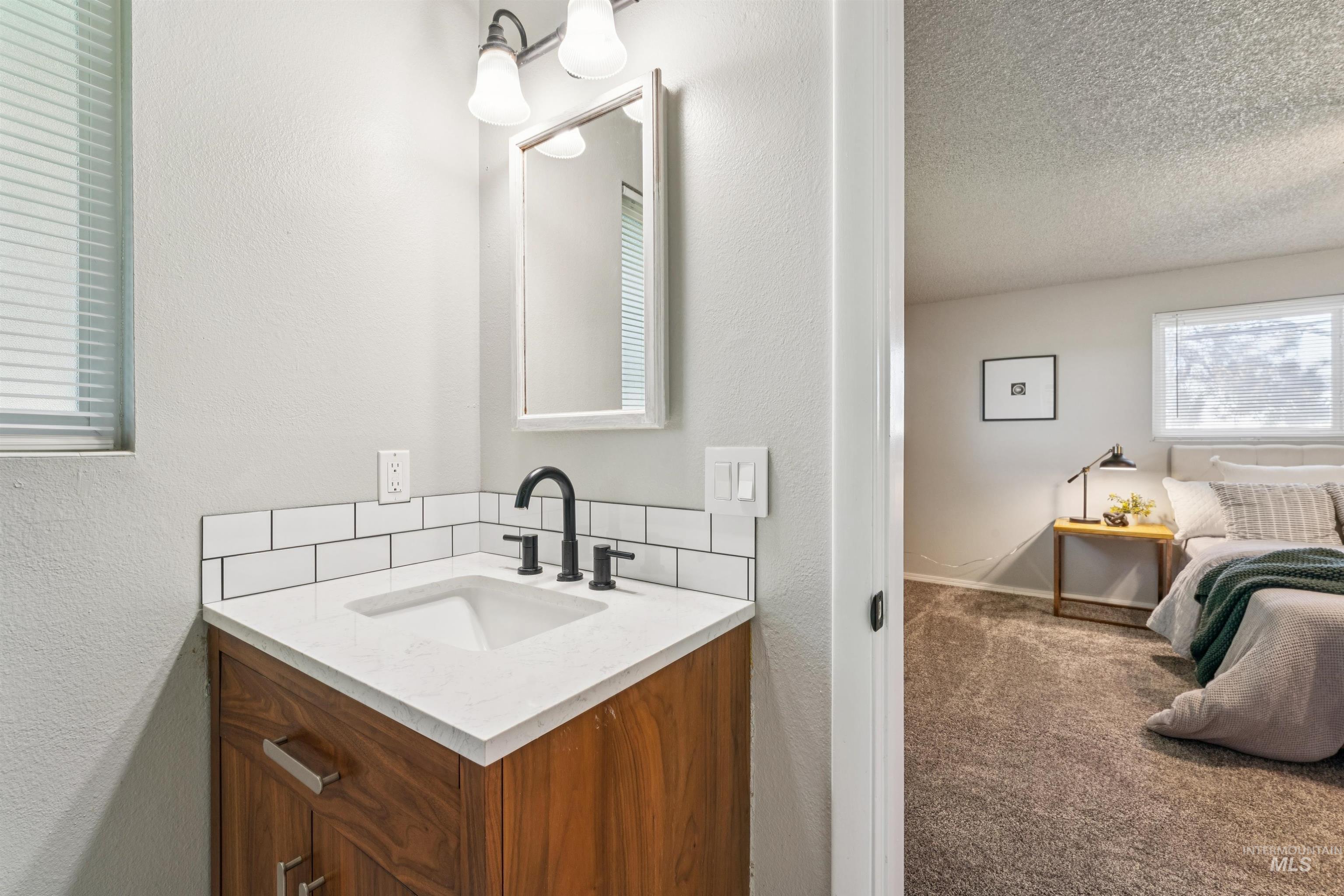 Bathroom with a textured wall, vanity, carpet, and a textured ceiling