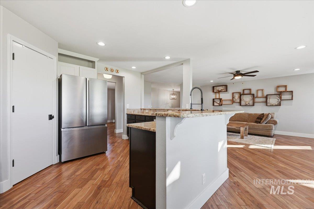 Kitchen with light stone counters, freestanding refrigerator, a ceiling fan, light wood finished floors, and recessed lighting