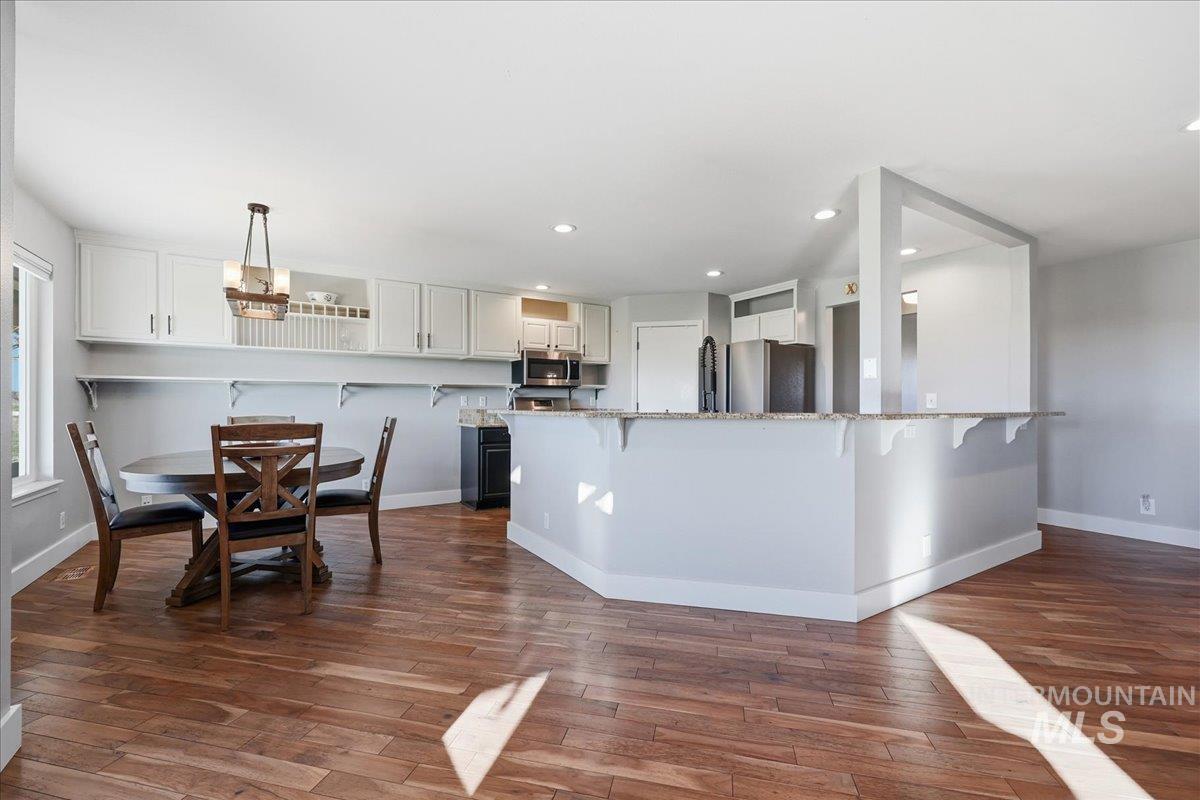 Kitchen featuring a kitchen breakfast bar, white cabinets, light stone countertops, appliances with stainless steel finishes, and dark wood-style flooring