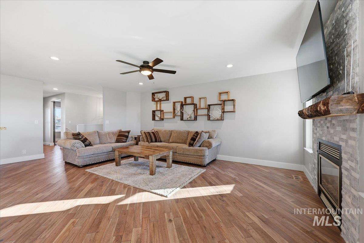 Living room featuring light wood-style floors, a glass covered fireplace, recessed lighting, and ceiling fan