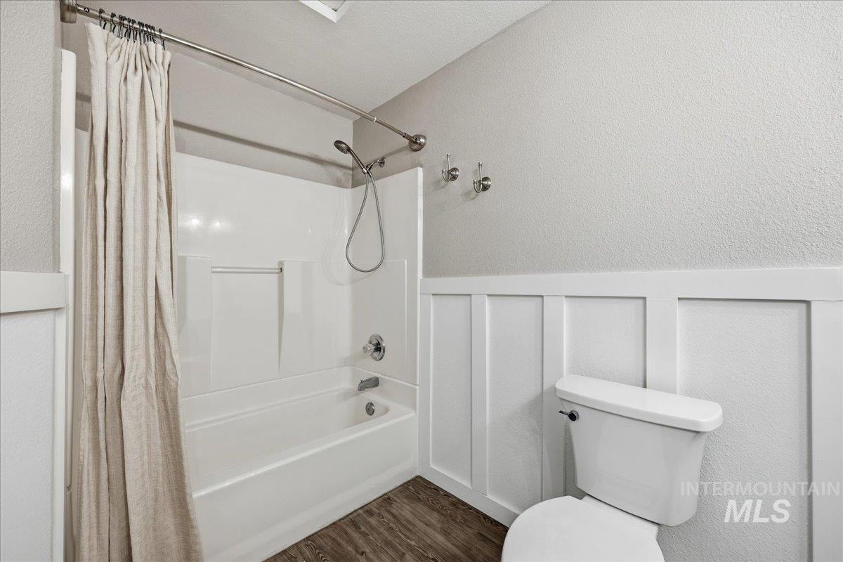 Full bathroom featuring shower / bath combination with curtain, a decorative wall, dark wood finished floors, a textured wall, and a wainscoted wall