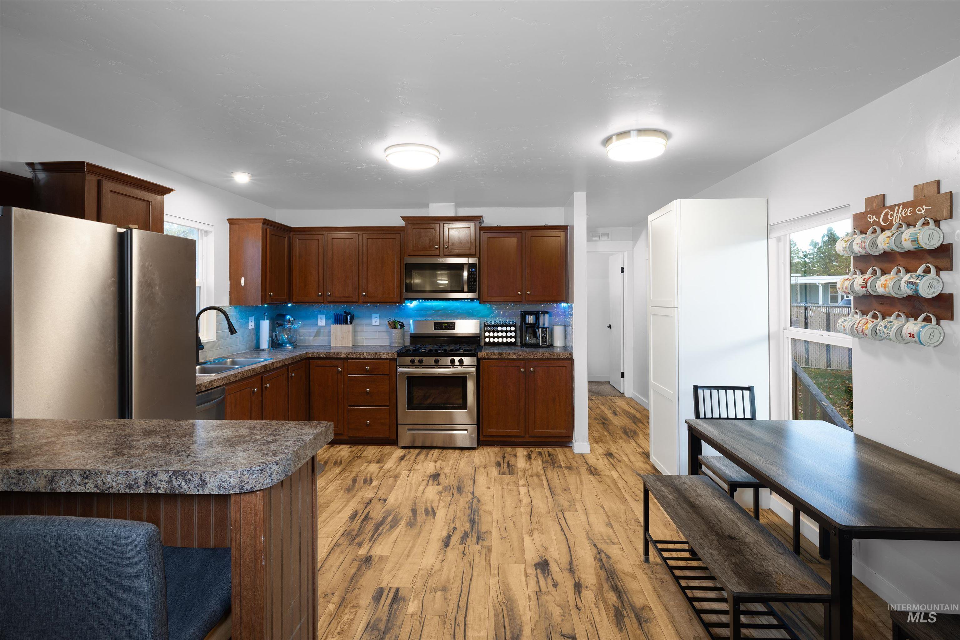Kitchen featuring darker countertops, breakfast bar, appliances with stainless steel finishes, gas stove, vinyl plank flooring, decorative backsplash, and dark brown cabinets.
