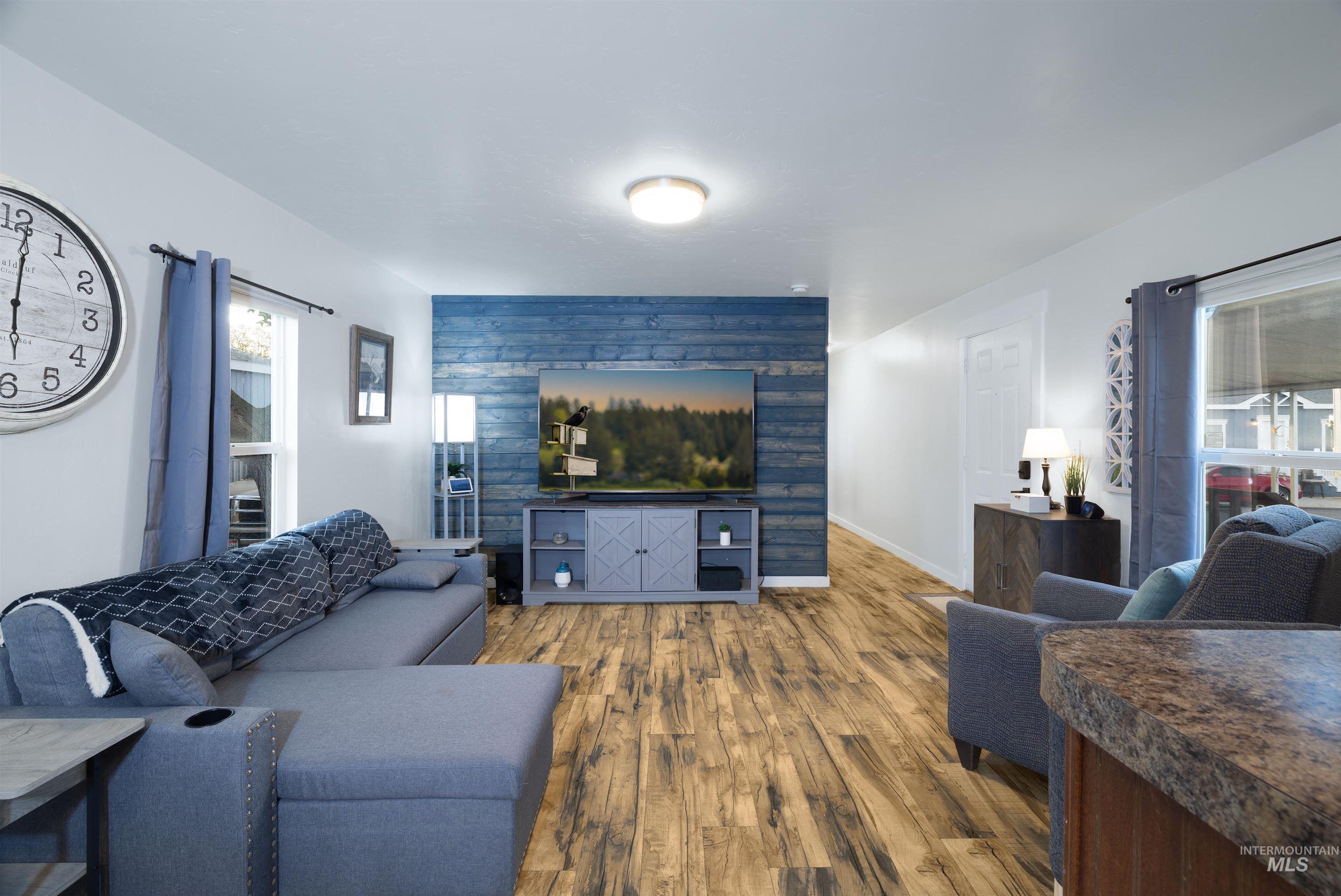 Living area featuring natural light, vinyl plank floors, baseboards and accent wall