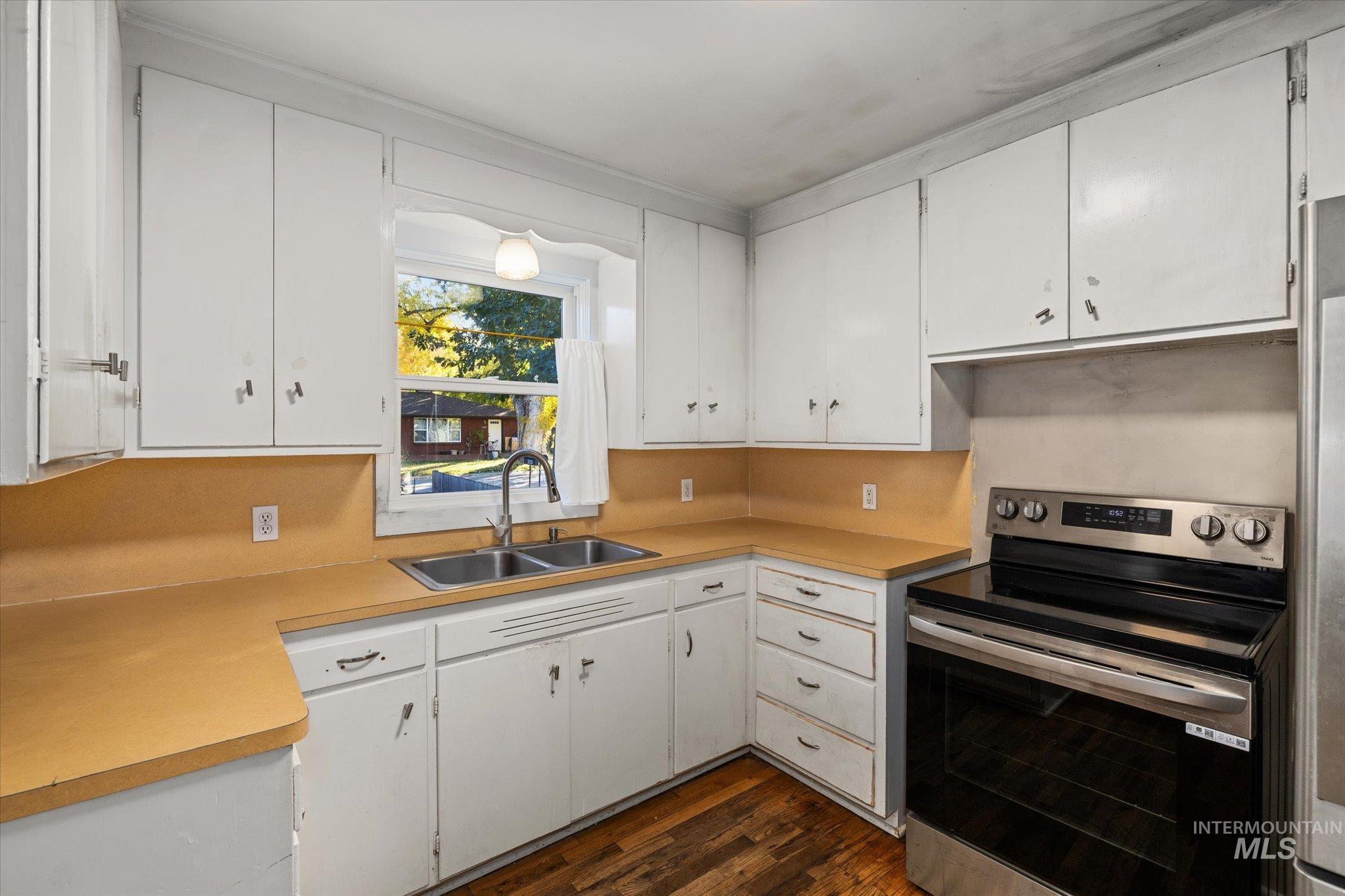 Kitchen featuring electric range, white cabinets, light countertops, and dark wood-style flooring