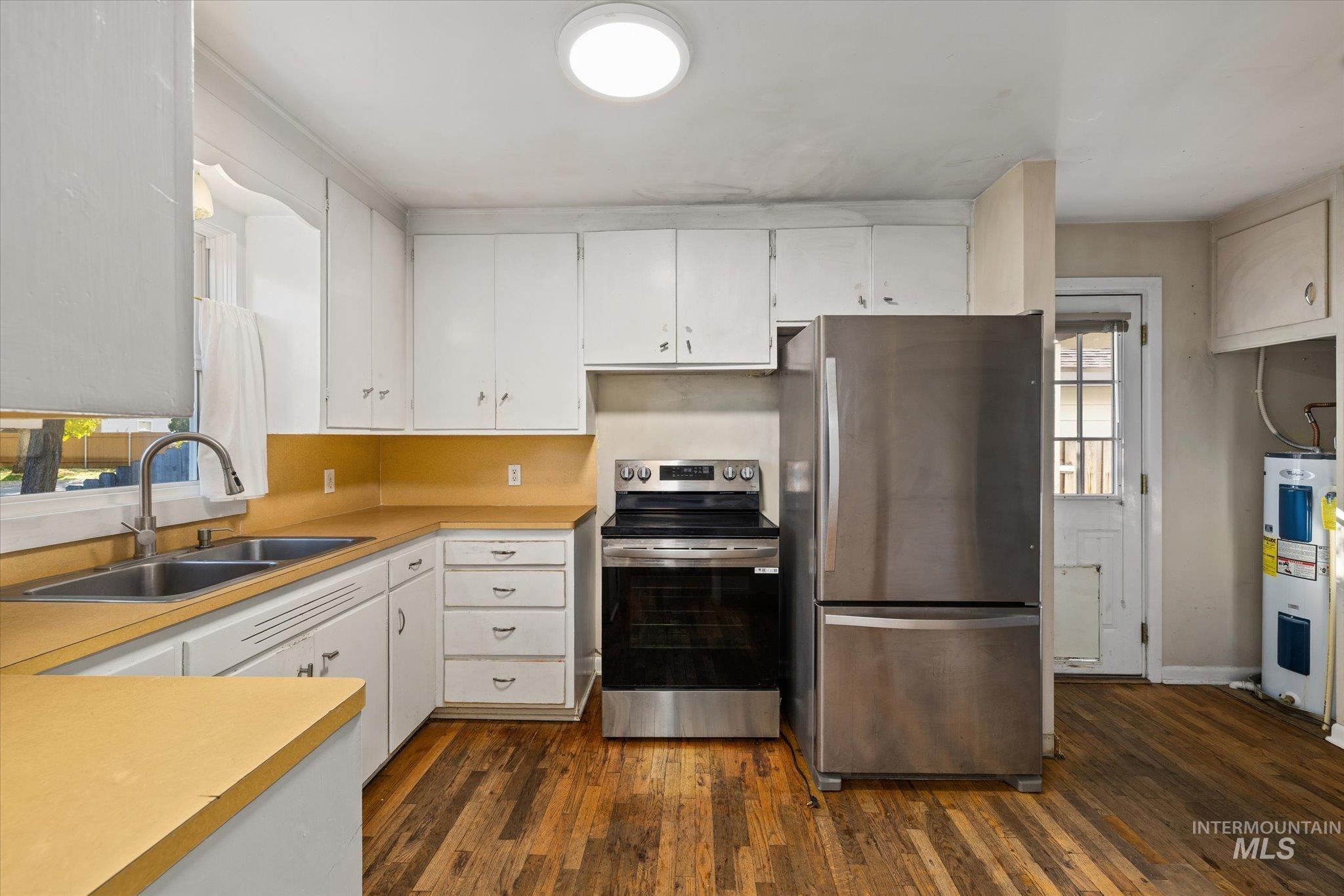Kitchen with appliances with stainless steel finishes, light countertops, dark wood-style flooring, water heater, and white cabinets