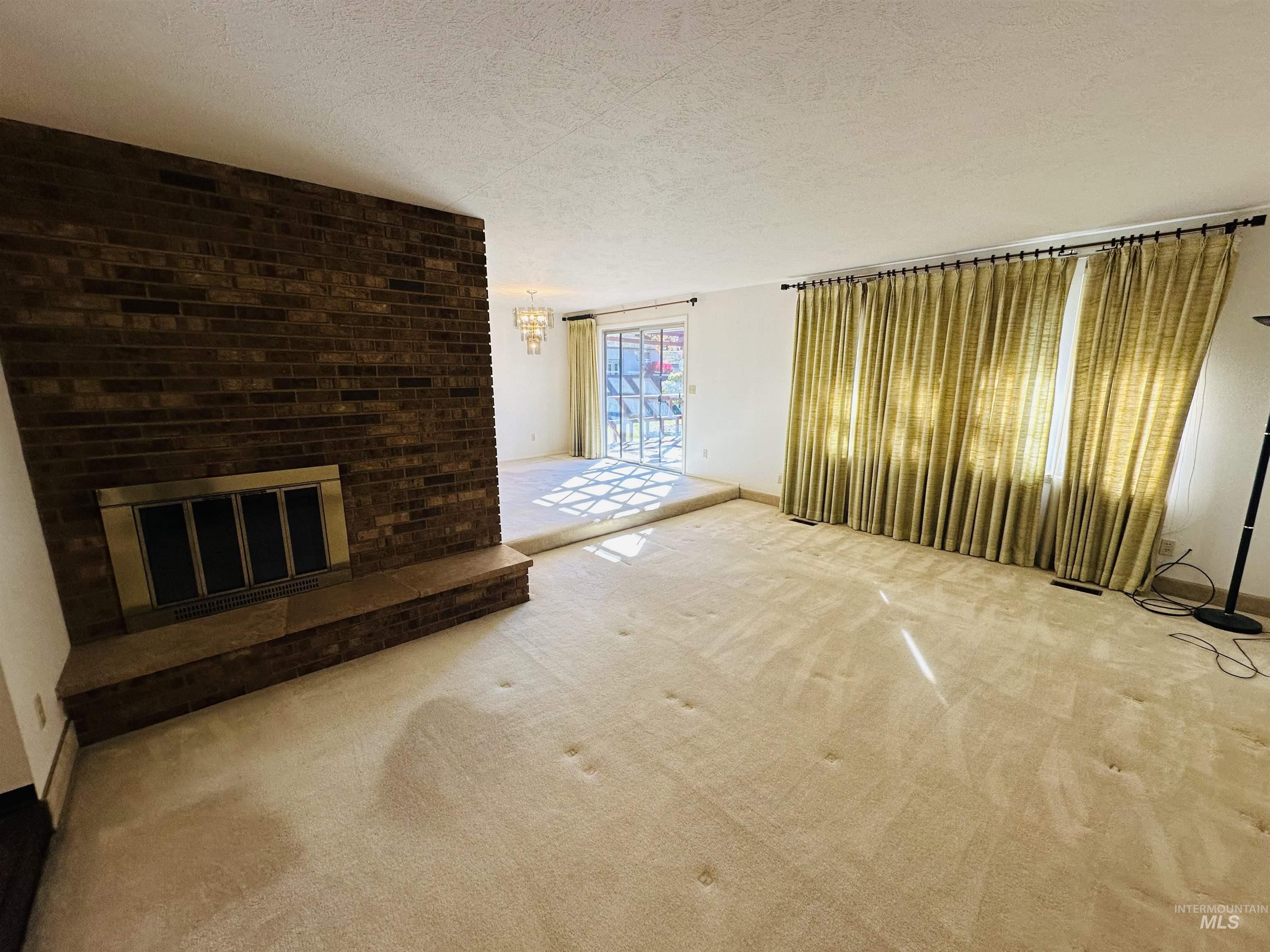 Unfurnished living room featuring a textured ceiling, carpet flooring, a fireplace, and a chandelier