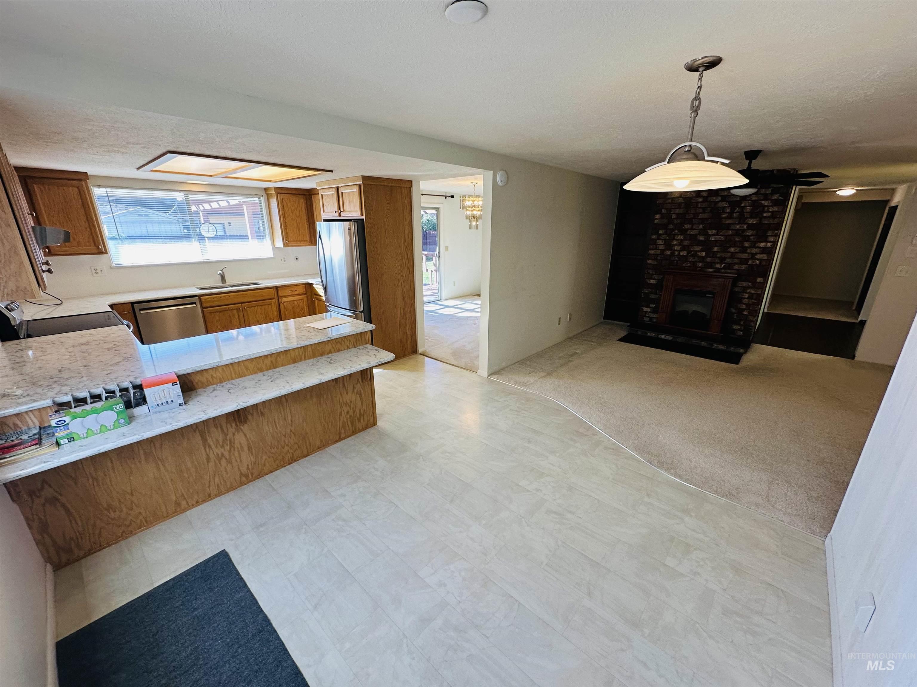 Kitchen featuring brown cabinetry, a fireplace, light colored carpet, decorative light fixtures, and appliances with stainless steel finishes