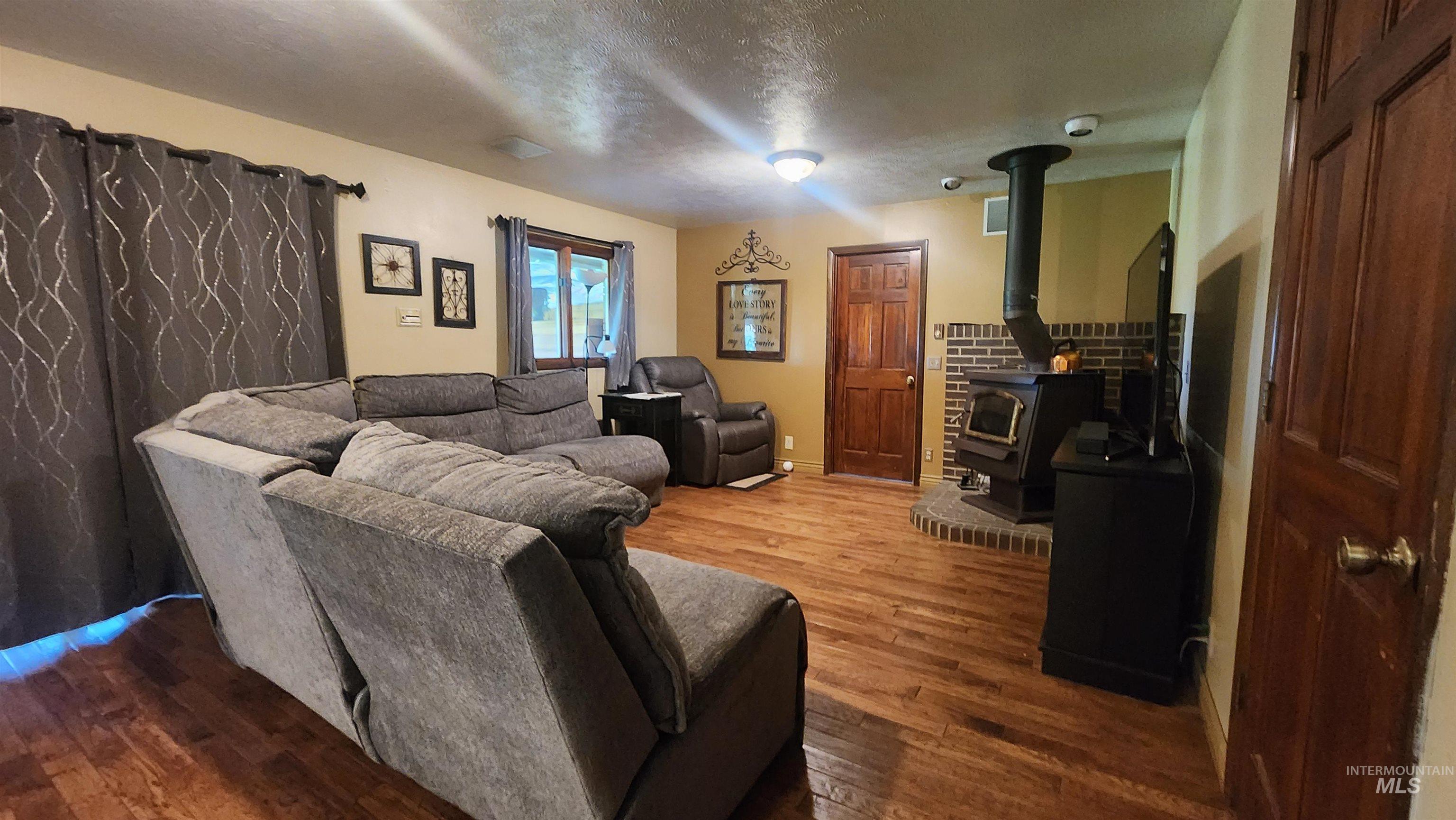 Living room featuring a wood stove, wood finished floors, and a textured ceiling