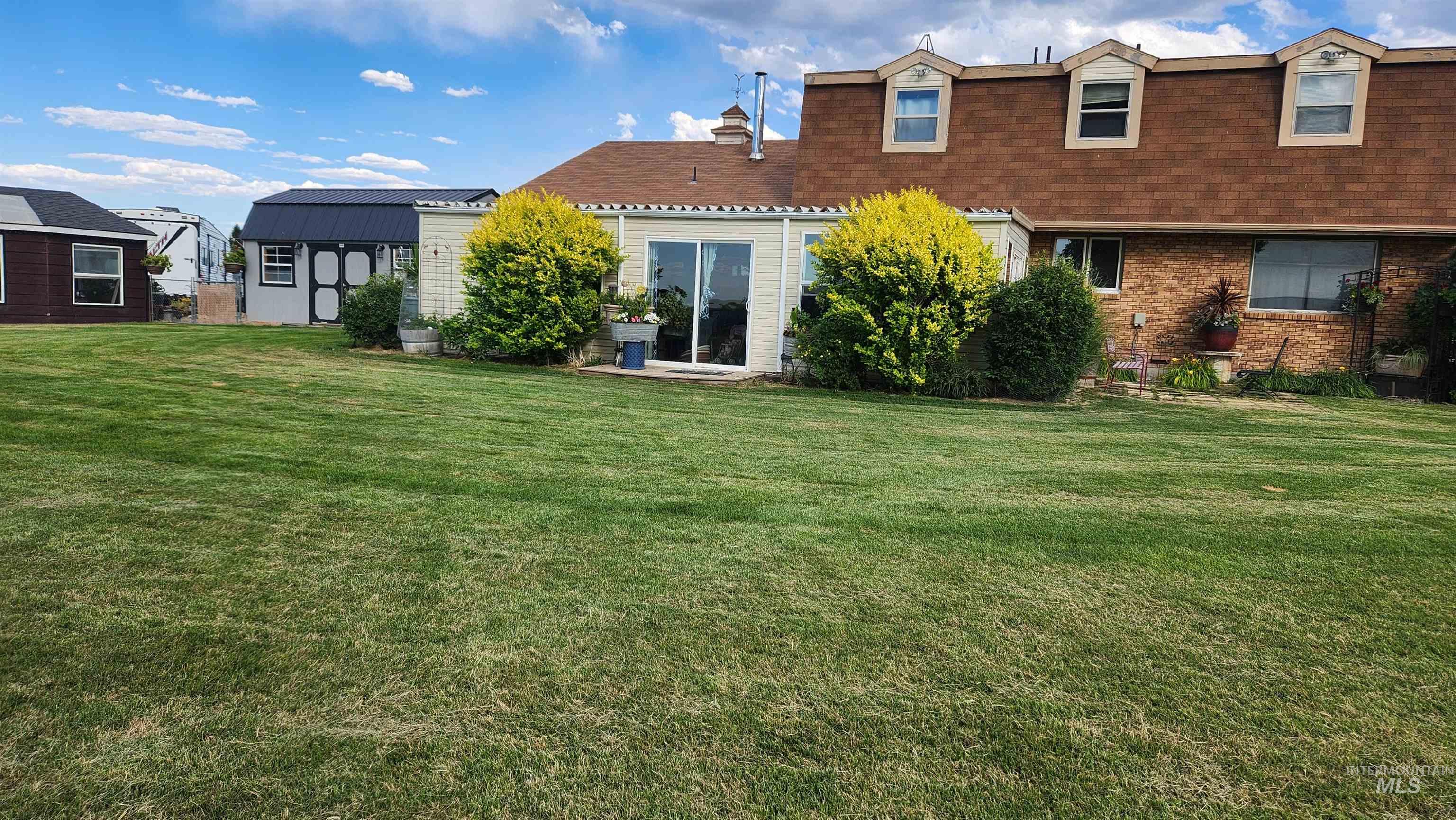 Back of house featuring a yard, brick siding, roof with shingles, and a storage unit