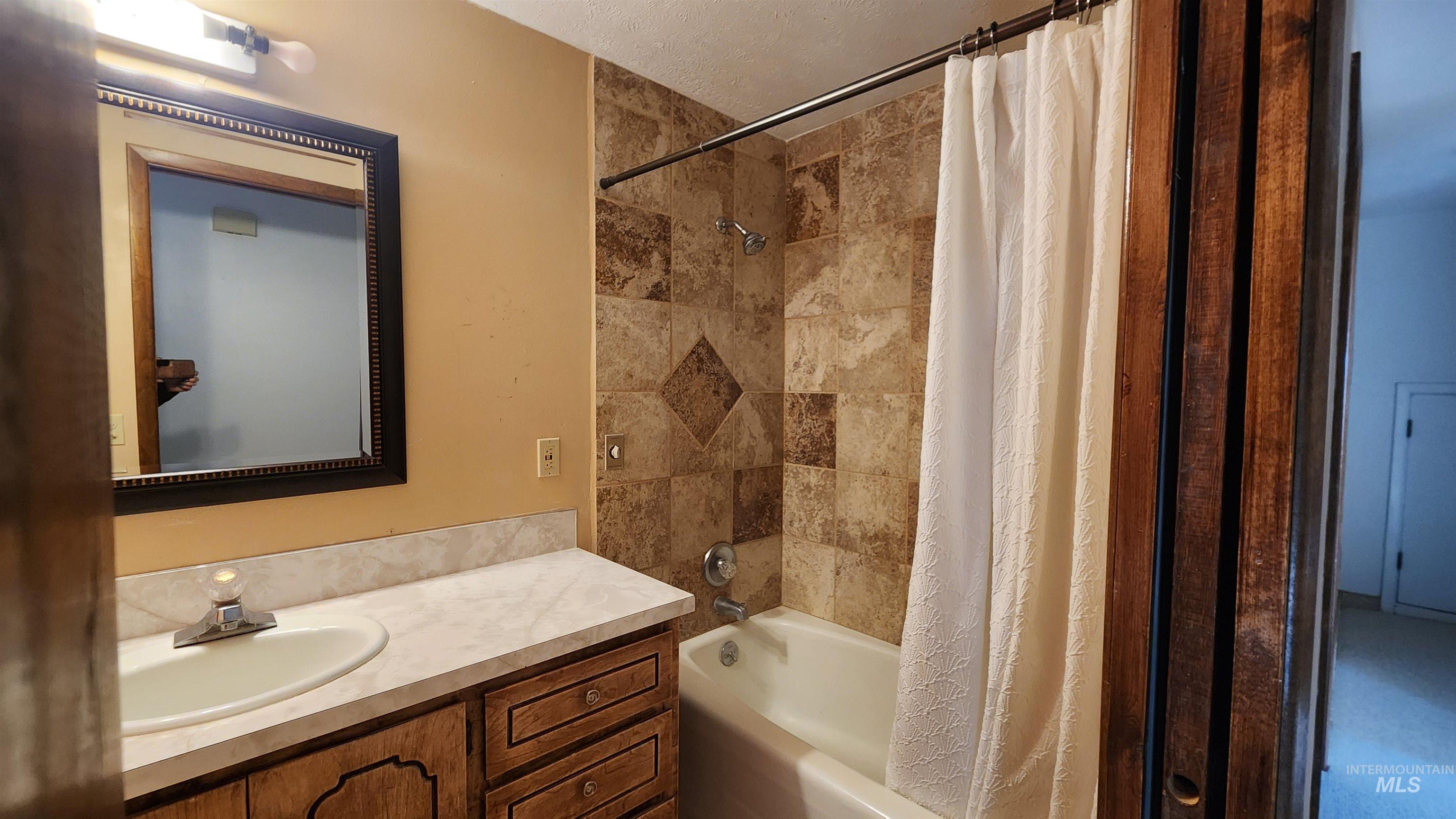 Full bathroom featuring shower / bath combo with tiled shower, vanity, and a textured ceiling