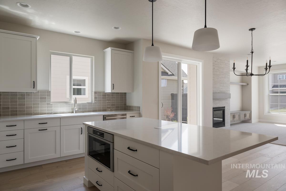 Kitchen featuring pendant lighting, light wood-style flooring, white cabinetry, and tasteful backsplash