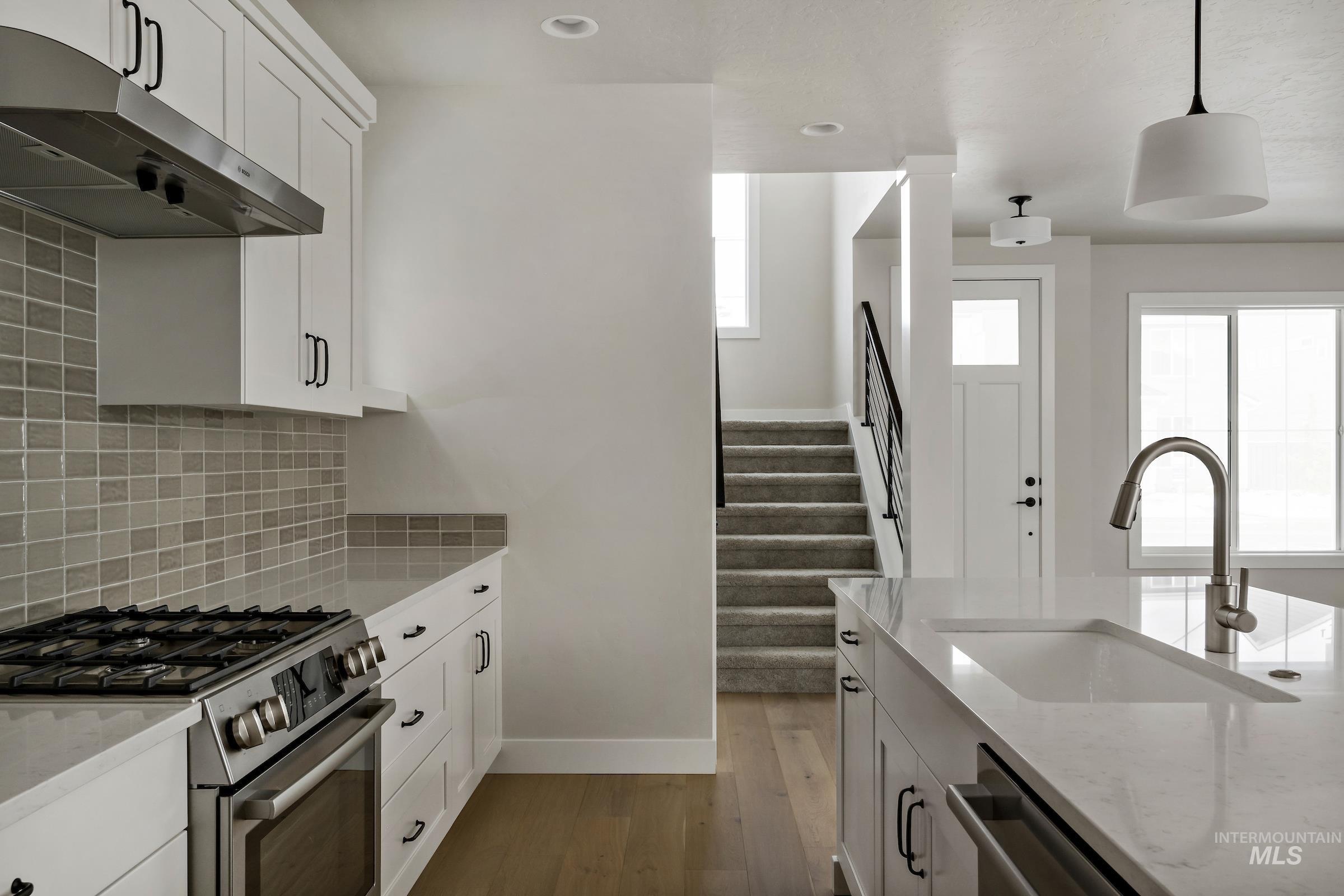 Kitchen with white cabinets, stainless steel appliances, light stone countertops, under cabinet range hood, and light wood finished floors