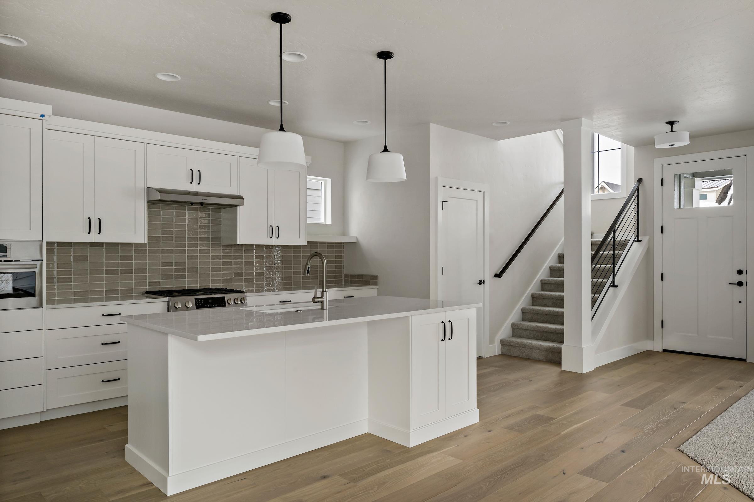 Kitchen with white cabinets, tasteful backsplash, a center island with sink, light wood-type flooring, and recessed lighting