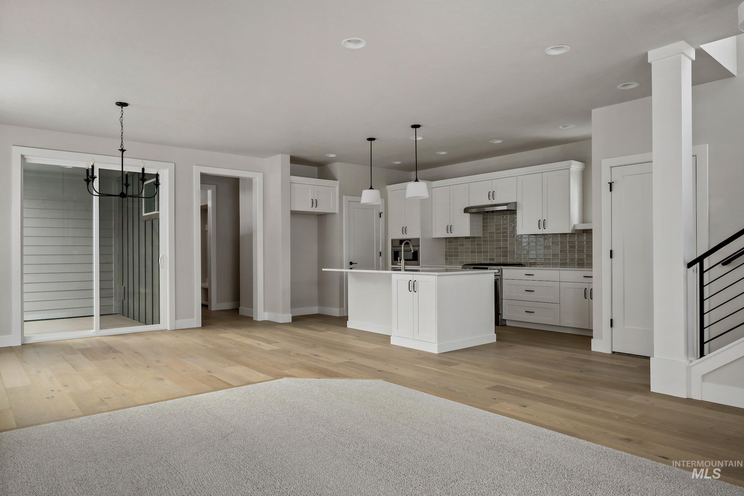 Kitchen featuring white cabinets, decorative backsplash, pendant lighting, stainless steel range with electric cooktop, and an island with sink