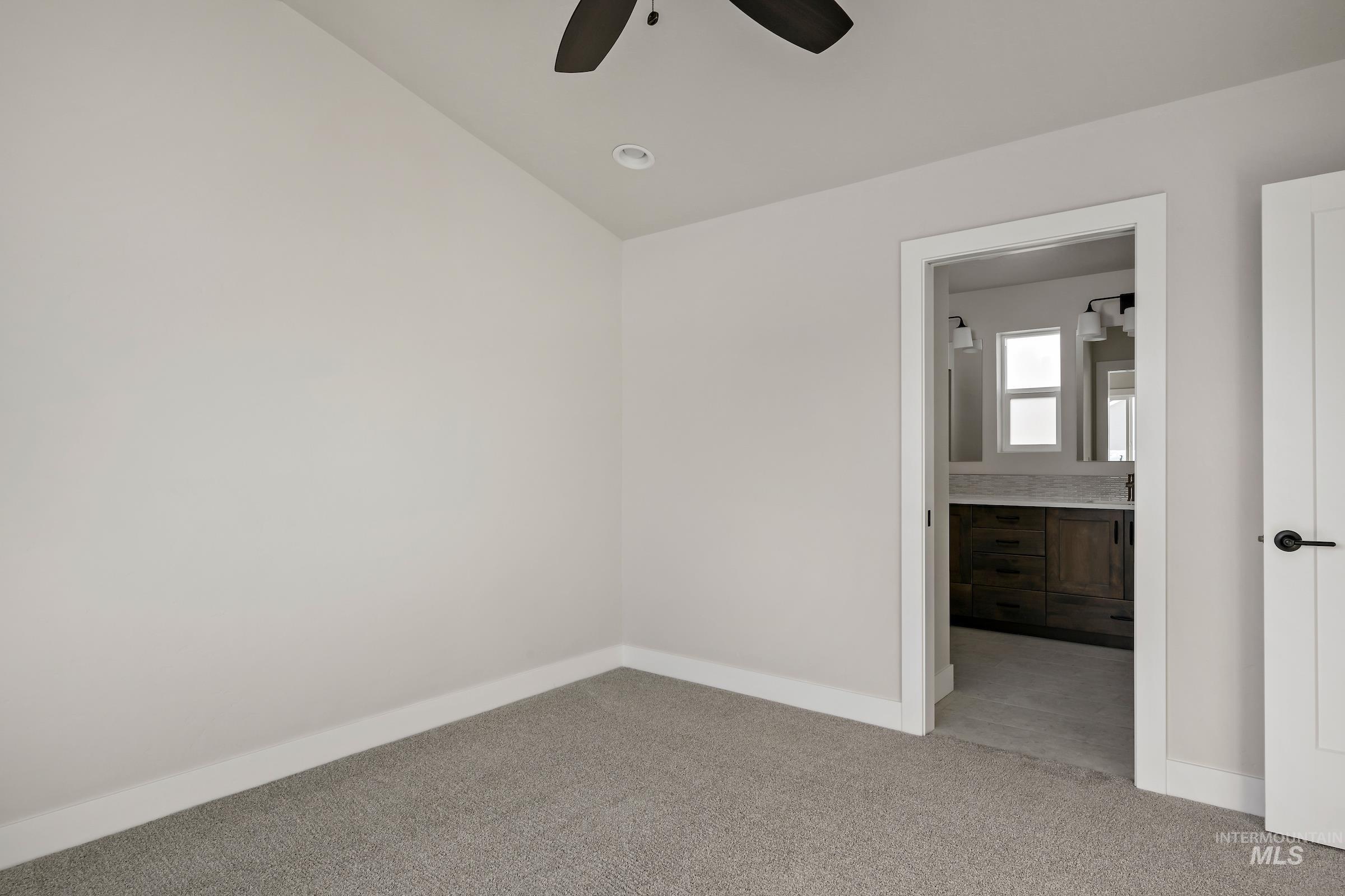 Unfurnished bedroom featuring light colored carpet, ensuite bath, and a ceiling fan