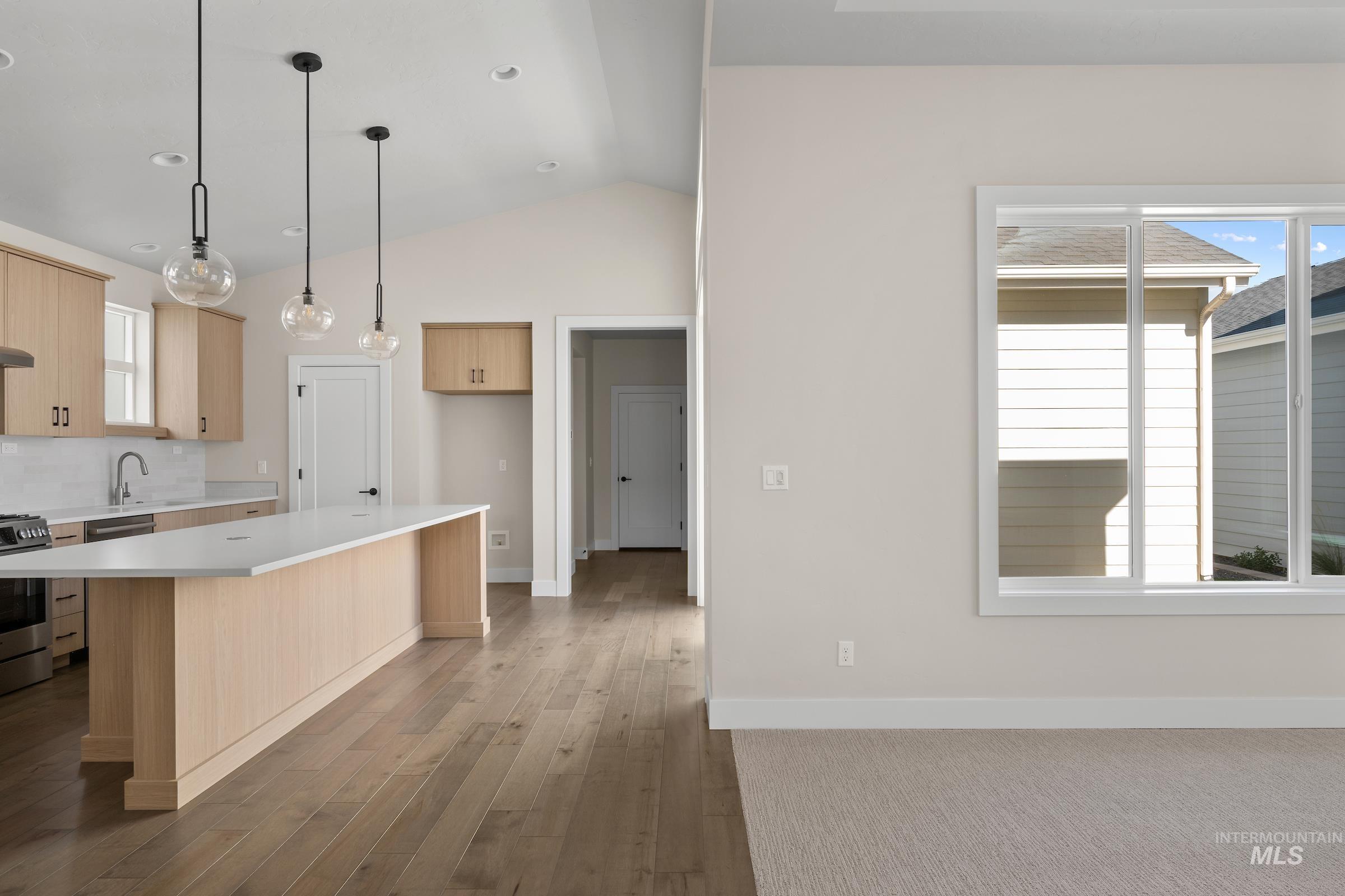 Kitchen with plenty of natural light, vaulted ceiling, pendant lighting, light brown cabinetry, and stainless steel gas range oven