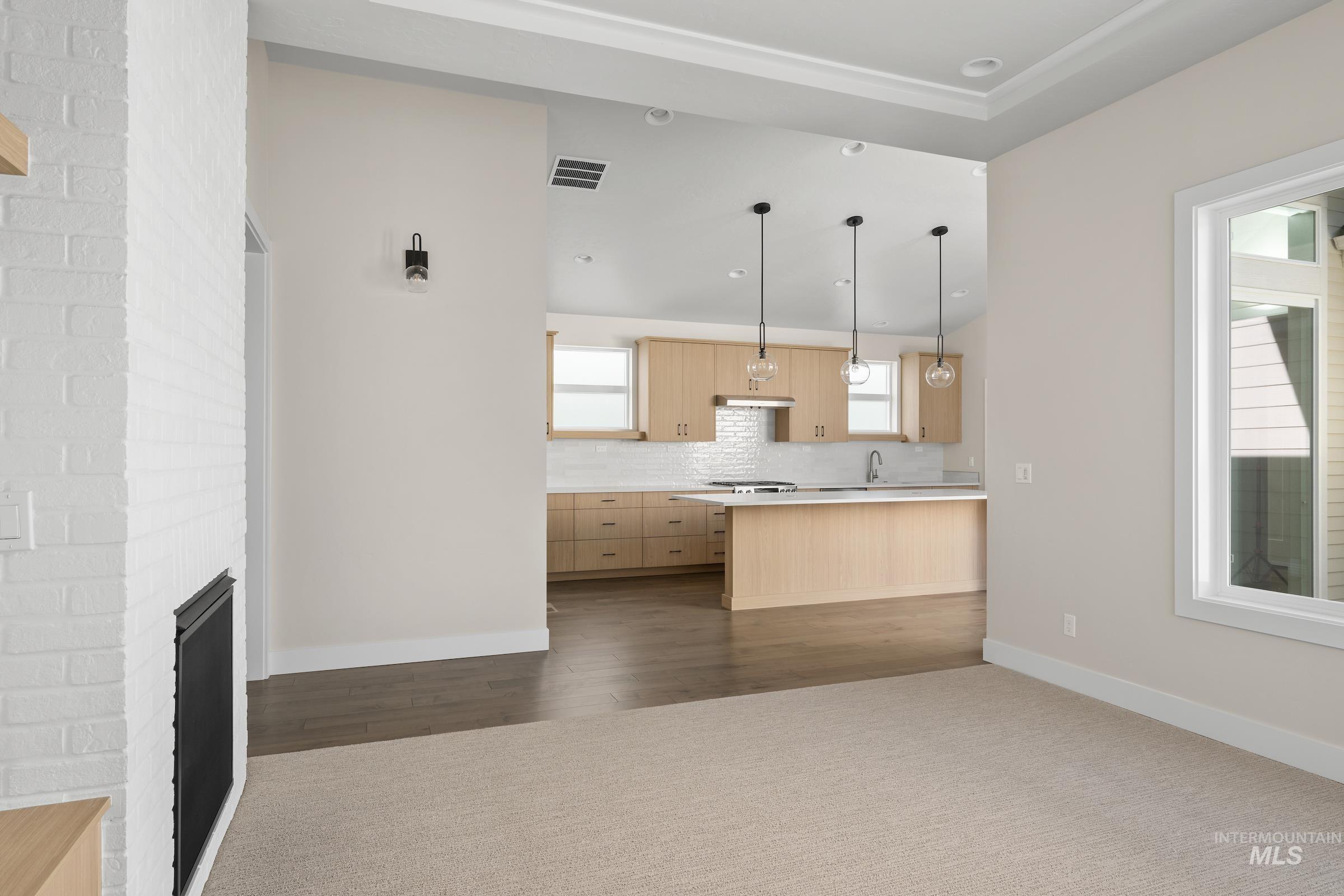 Kitchen featuring light brown cabinets, pendant lighting, light countertops, tasteful backsplash, and a brick fireplace