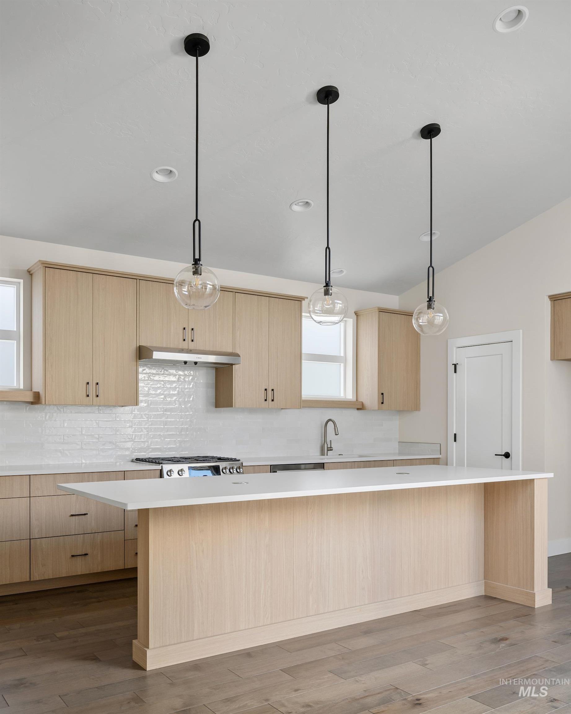 Kitchen featuring tasteful backsplash, light brown cabinets, decorative light fixtures, light wood-type flooring, and a center island