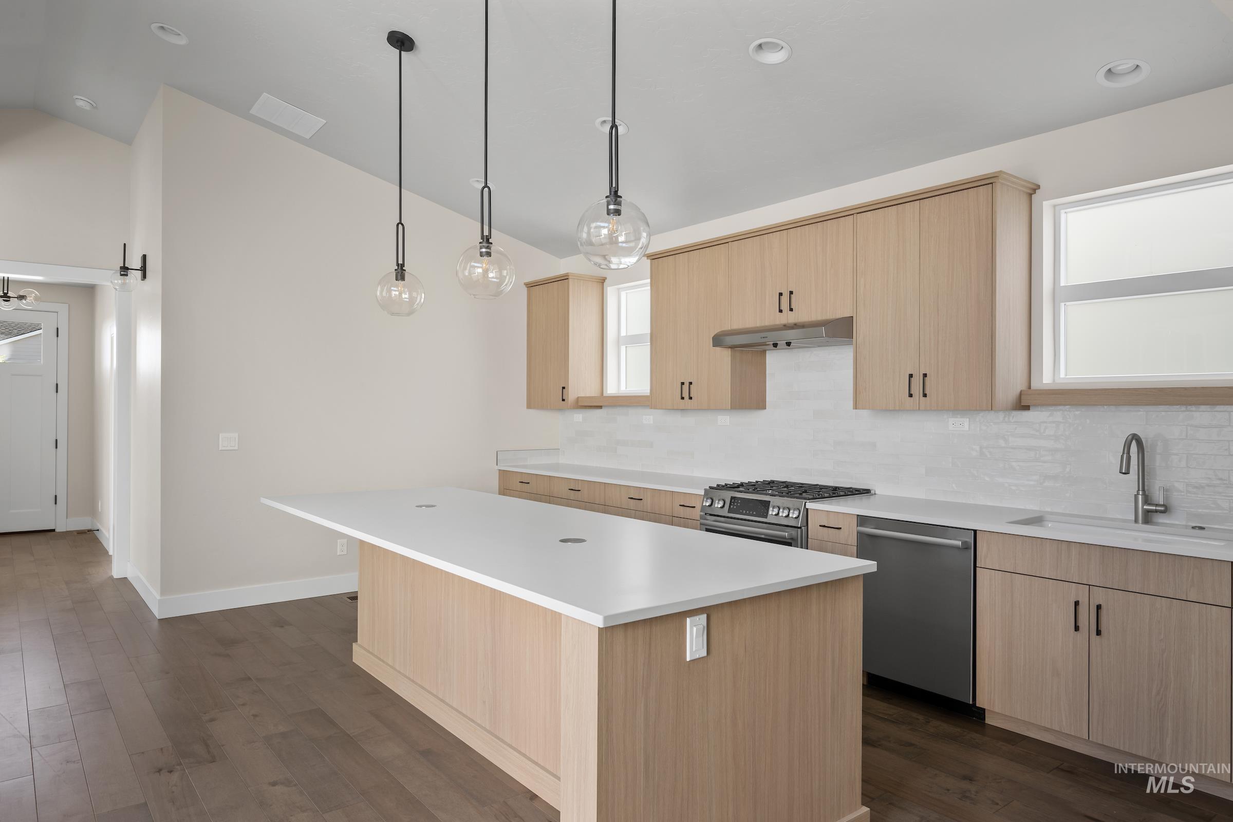 Kitchen with light brown cabinets, a barn door, dark wood finished floors, a center island, and lofted ceiling