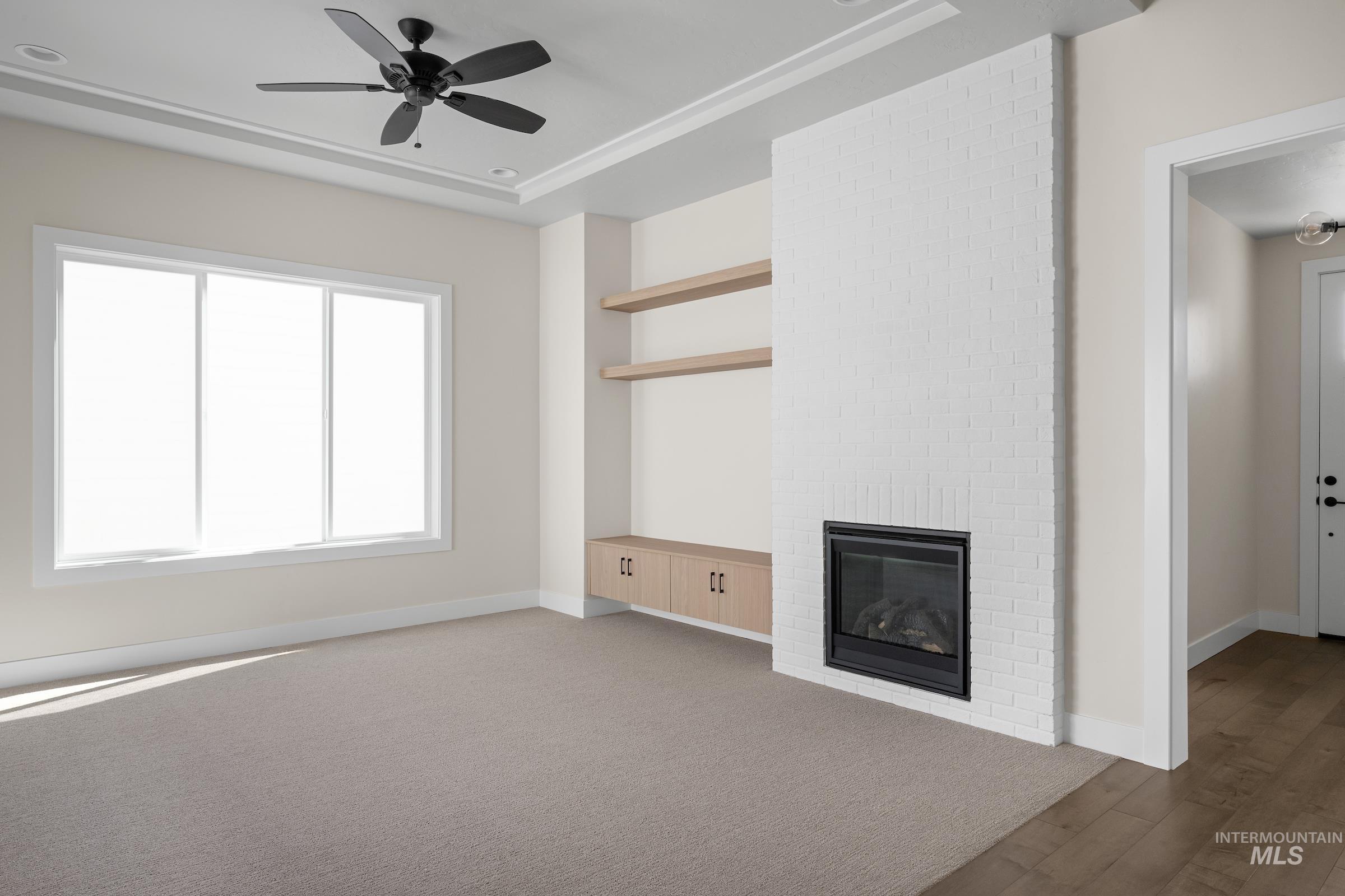 Unfurnished living room featuring a fireplace, ceiling fan, a raised ceiling, and wood finished floors