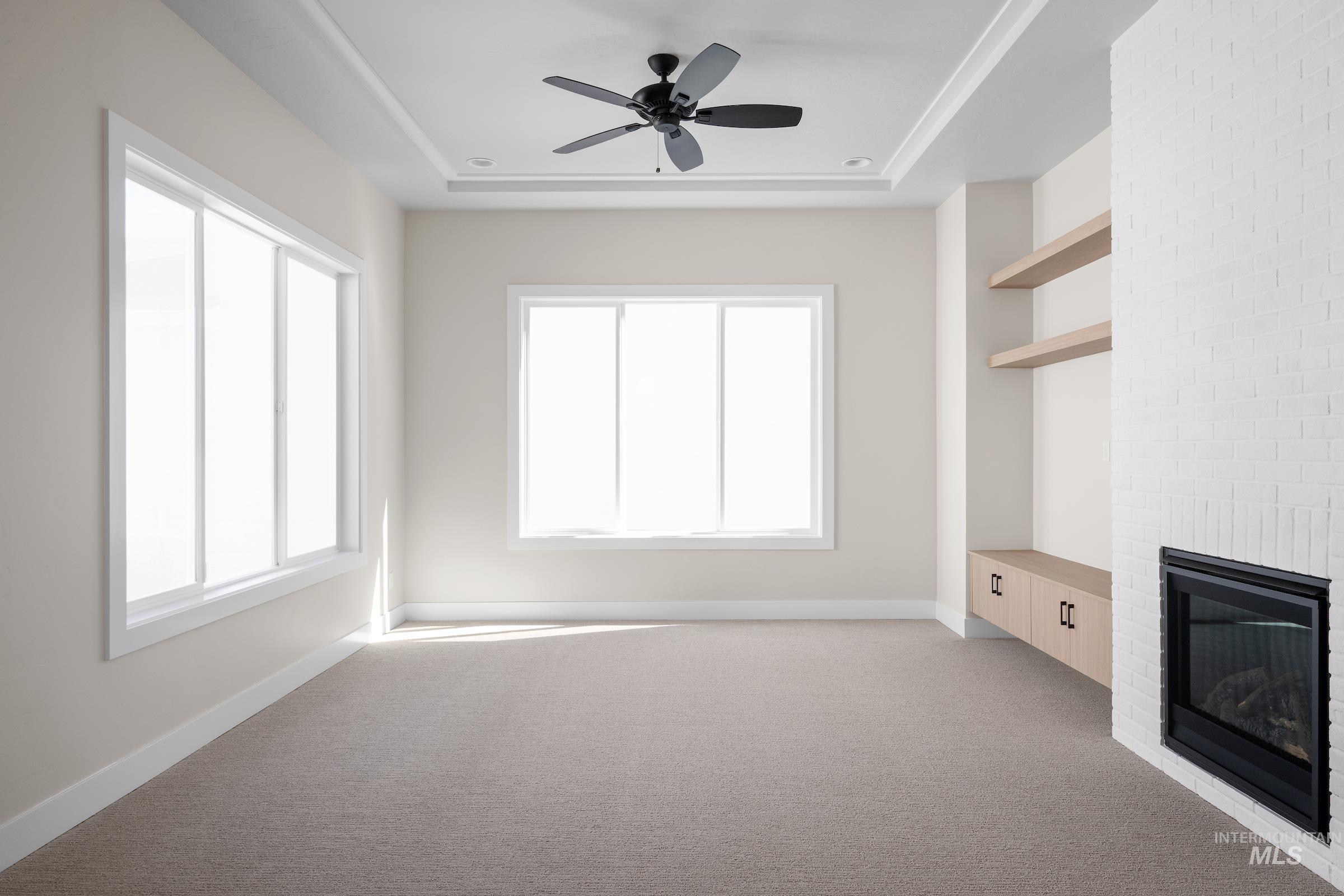 Unfurnished living room with a brick fireplace, light colored carpet, ceiling fan, and a raised ceiling