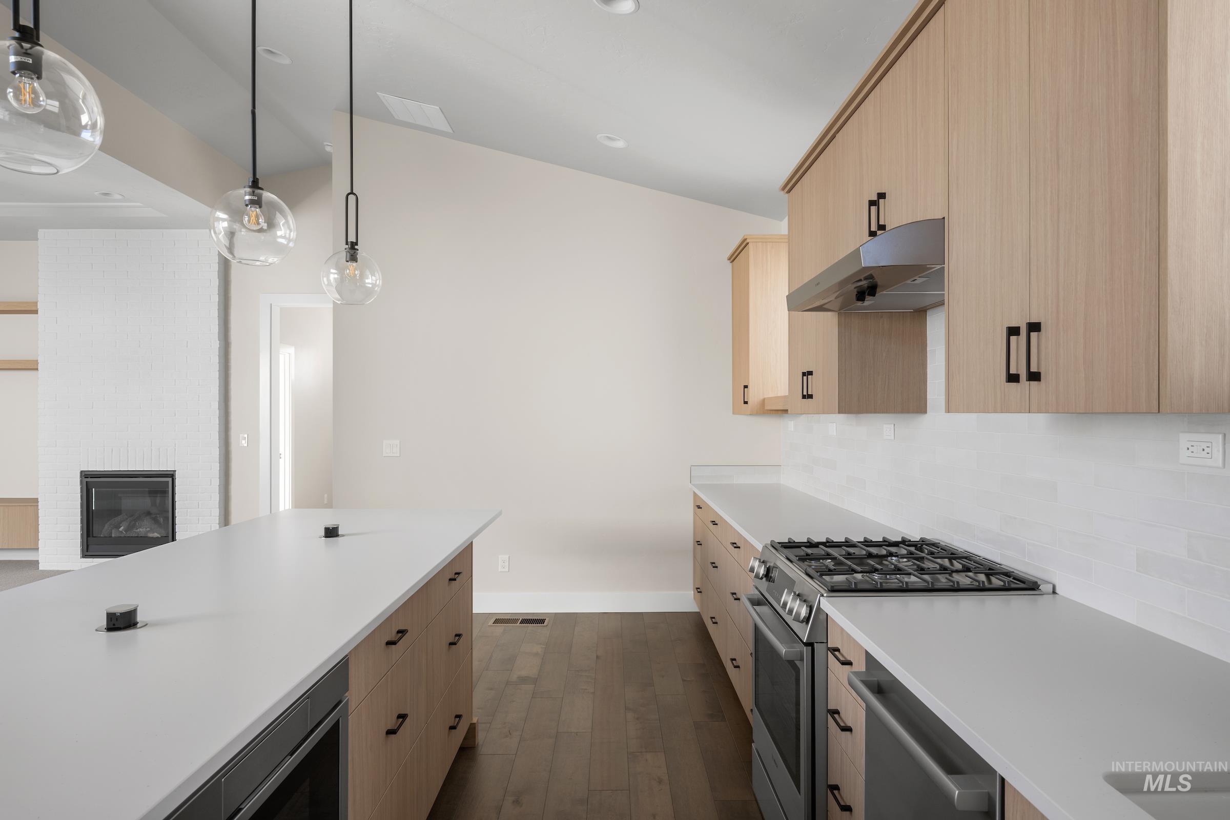 Kitchen with light brown cabinets, appliances with stainless steel finishes, decorative light fixtures, dark wood finished floors, and under cabinet range hood