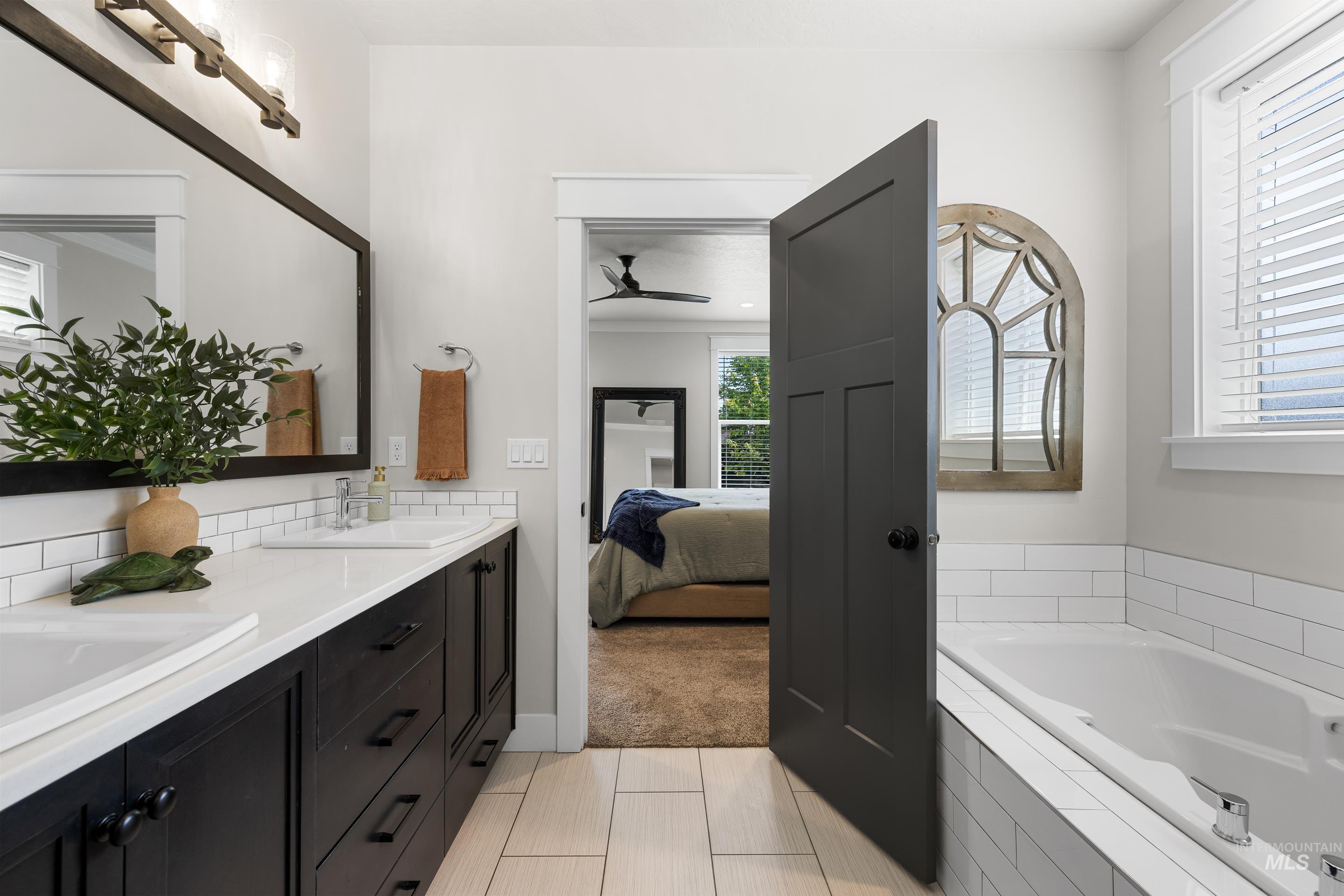 Ensuite bathroom featuring double vanity, a garden tub, tile patterned flooring, and a ceiling fan