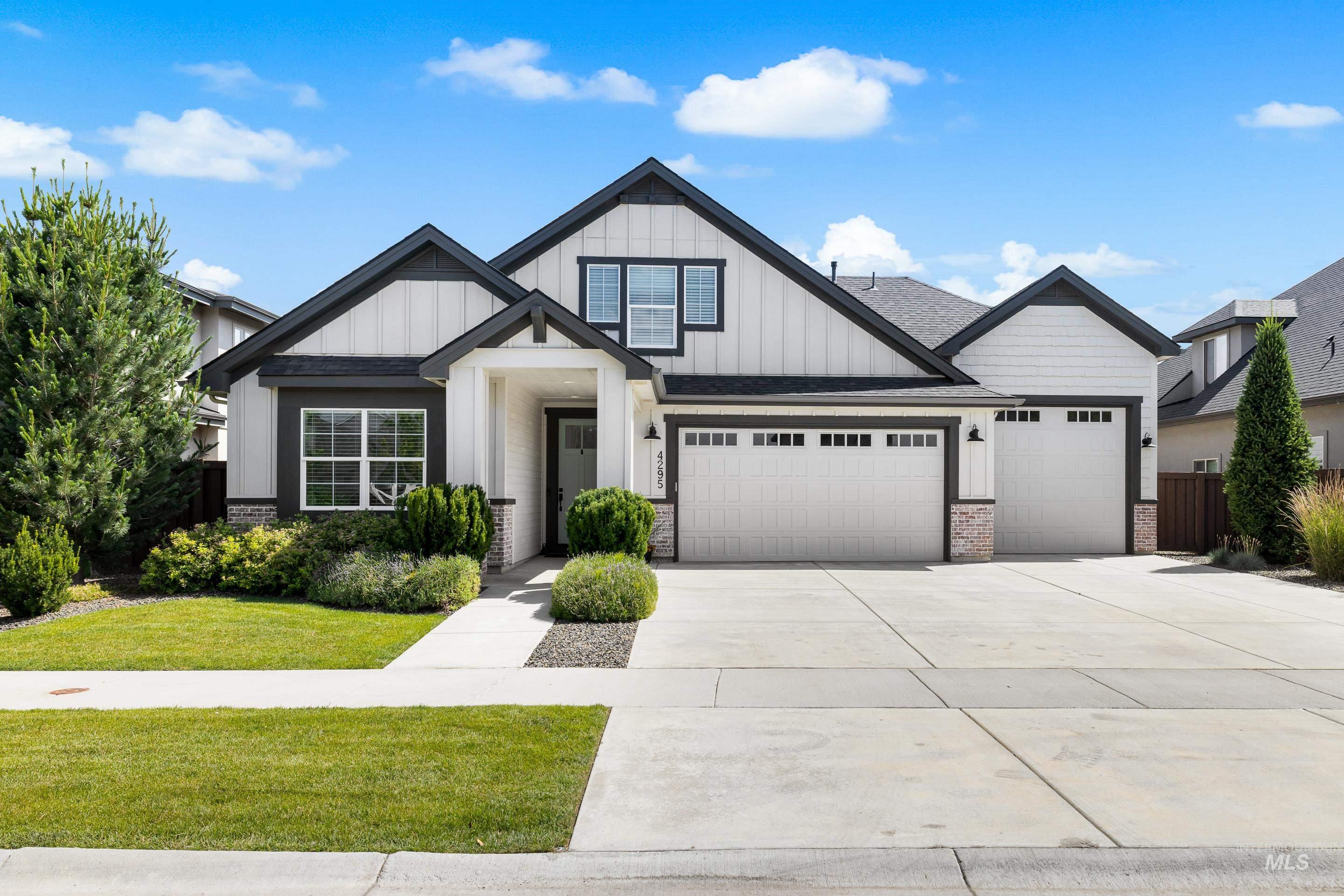View of front facade with board and batten siding, brick siding, a garage, driveway, and a shingled roof