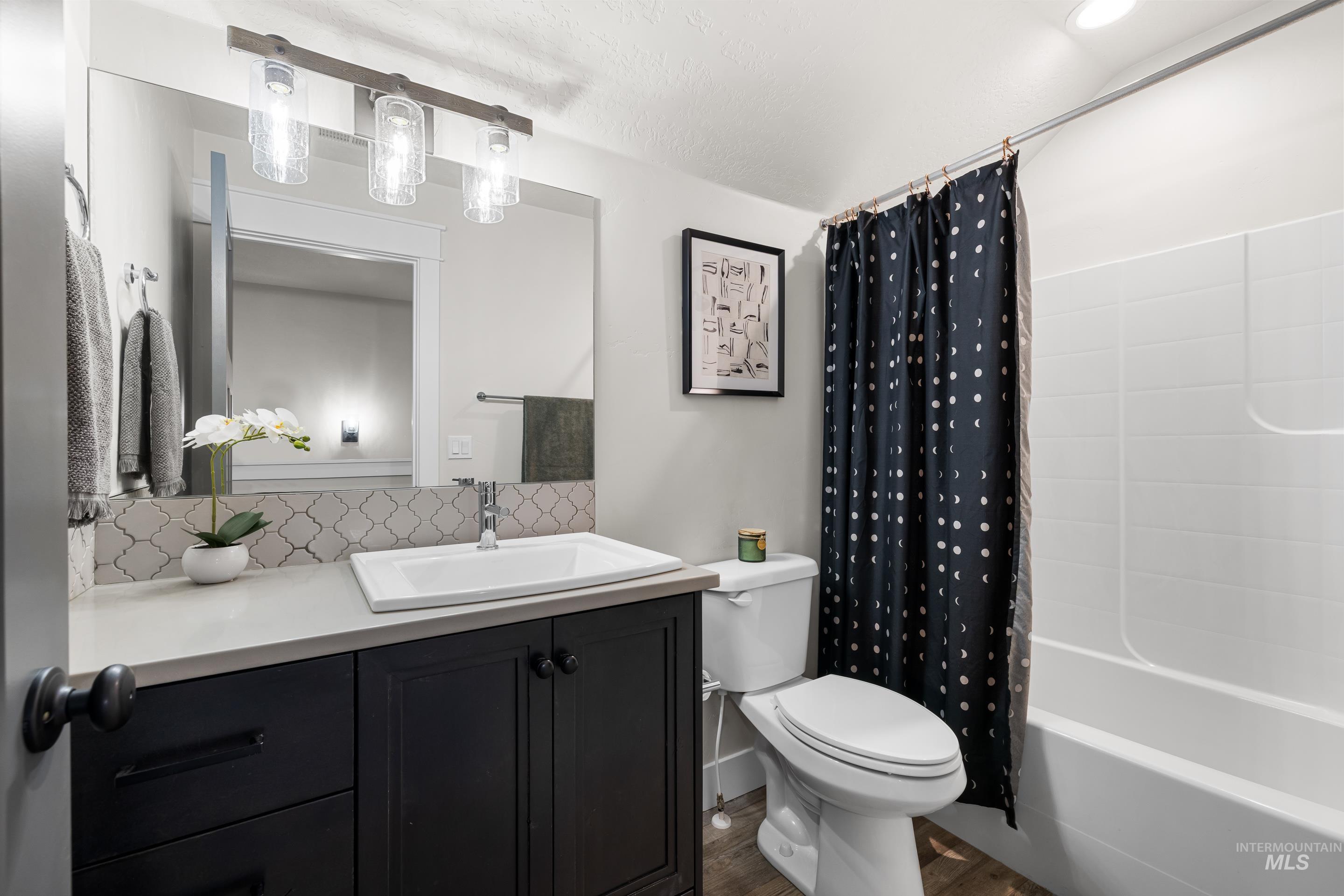 Bathroom featuring wood finished floors, backsplash, vanity, and shower / bath combo with shower curtain