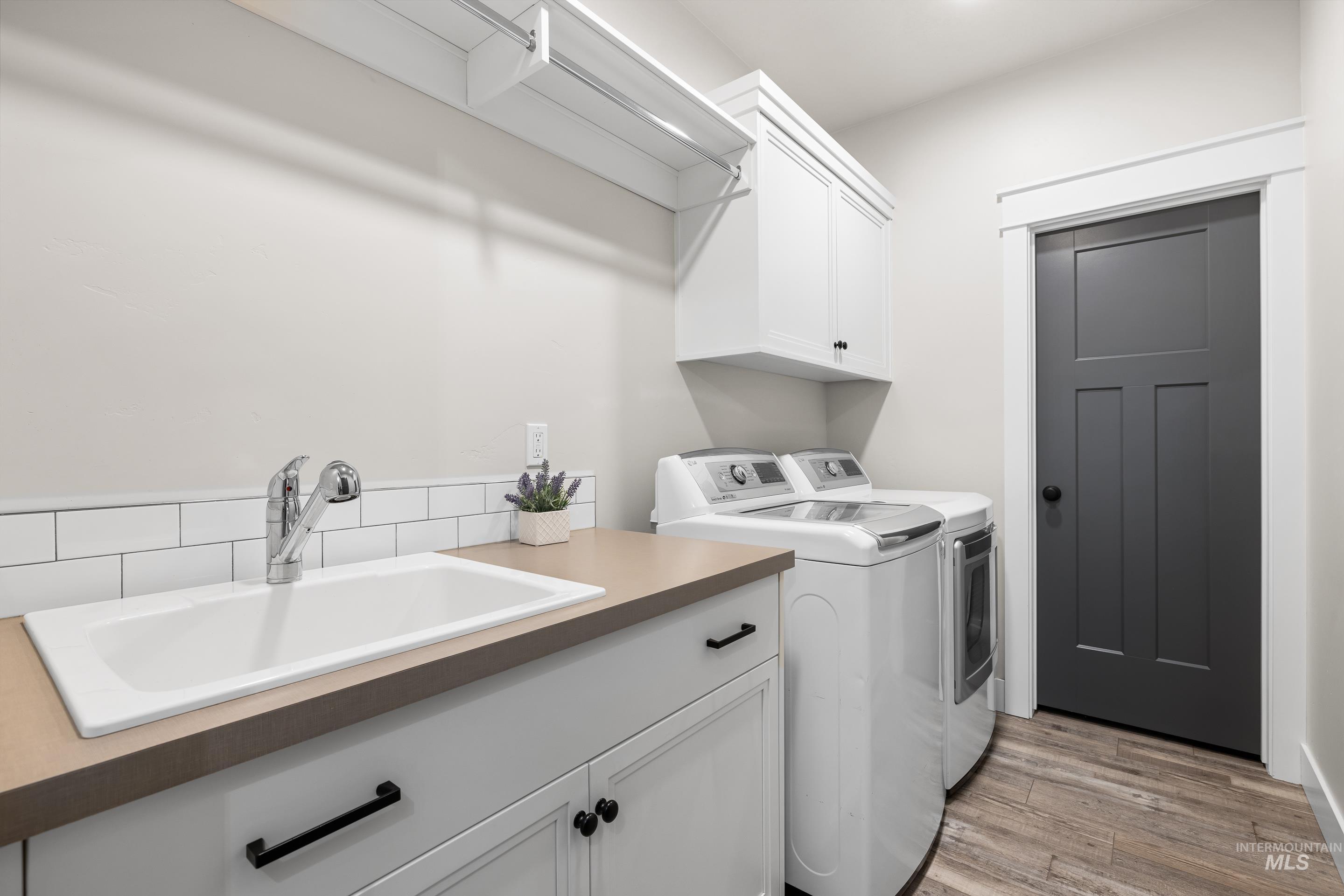 Laundry room with independent washer and dryer, cabinet space, and light wood-style flooring