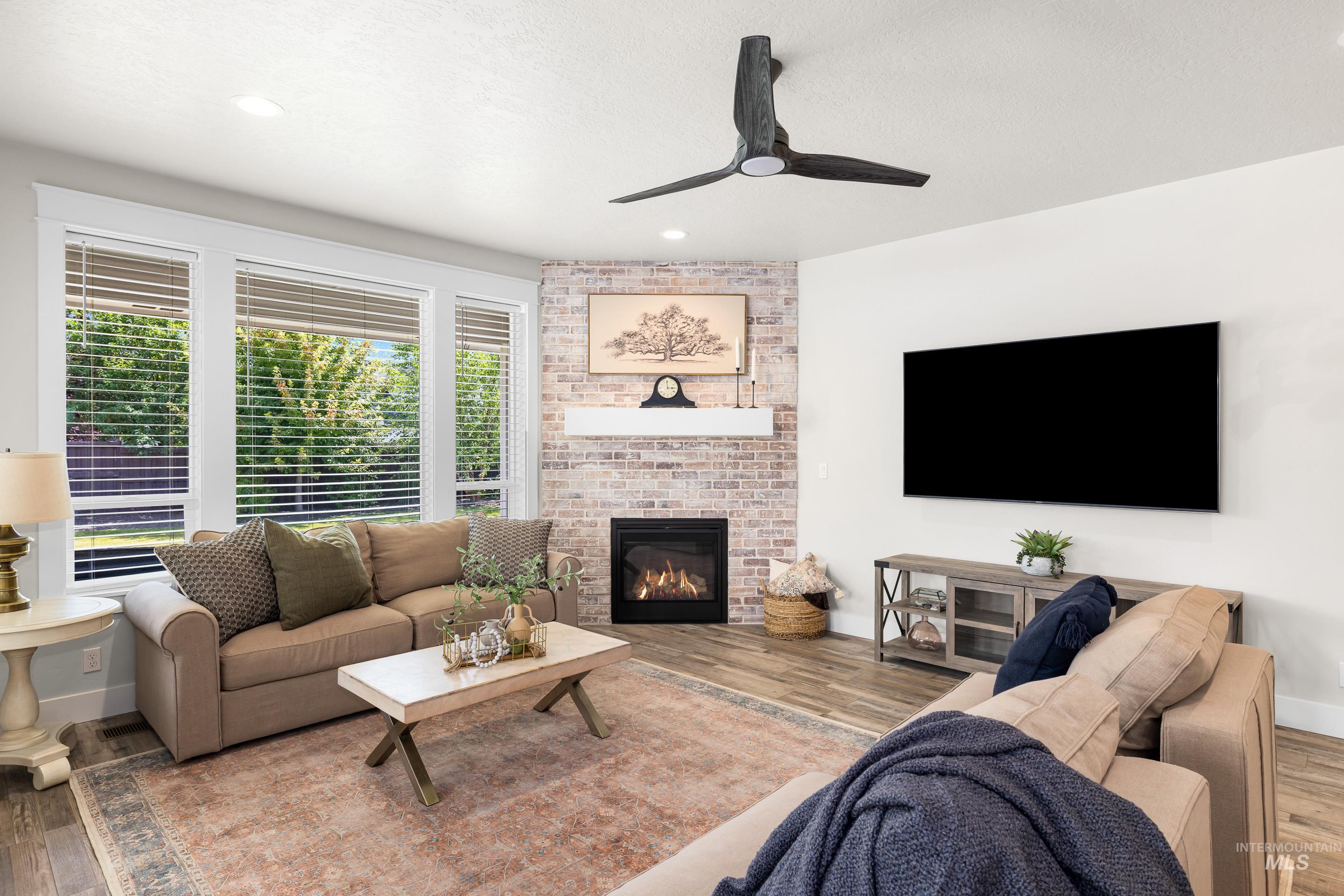 Living room with a ceiling fan, wood finished floors, a fireplace, and recessed lighting