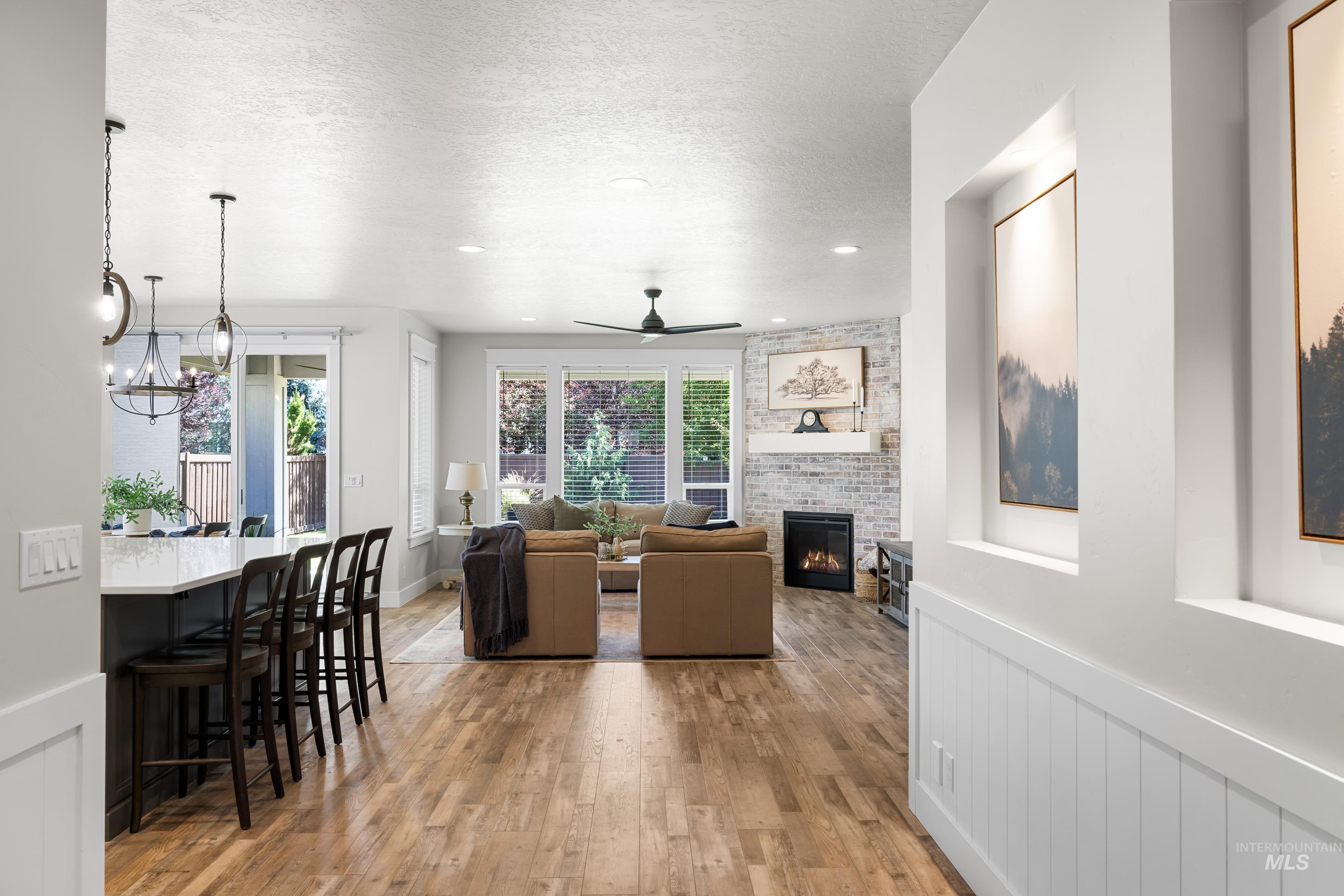 Dining area featuring a ceiling fan, a large fireplace, light wood-style flooring, a wainscoted wall, and a chandelier