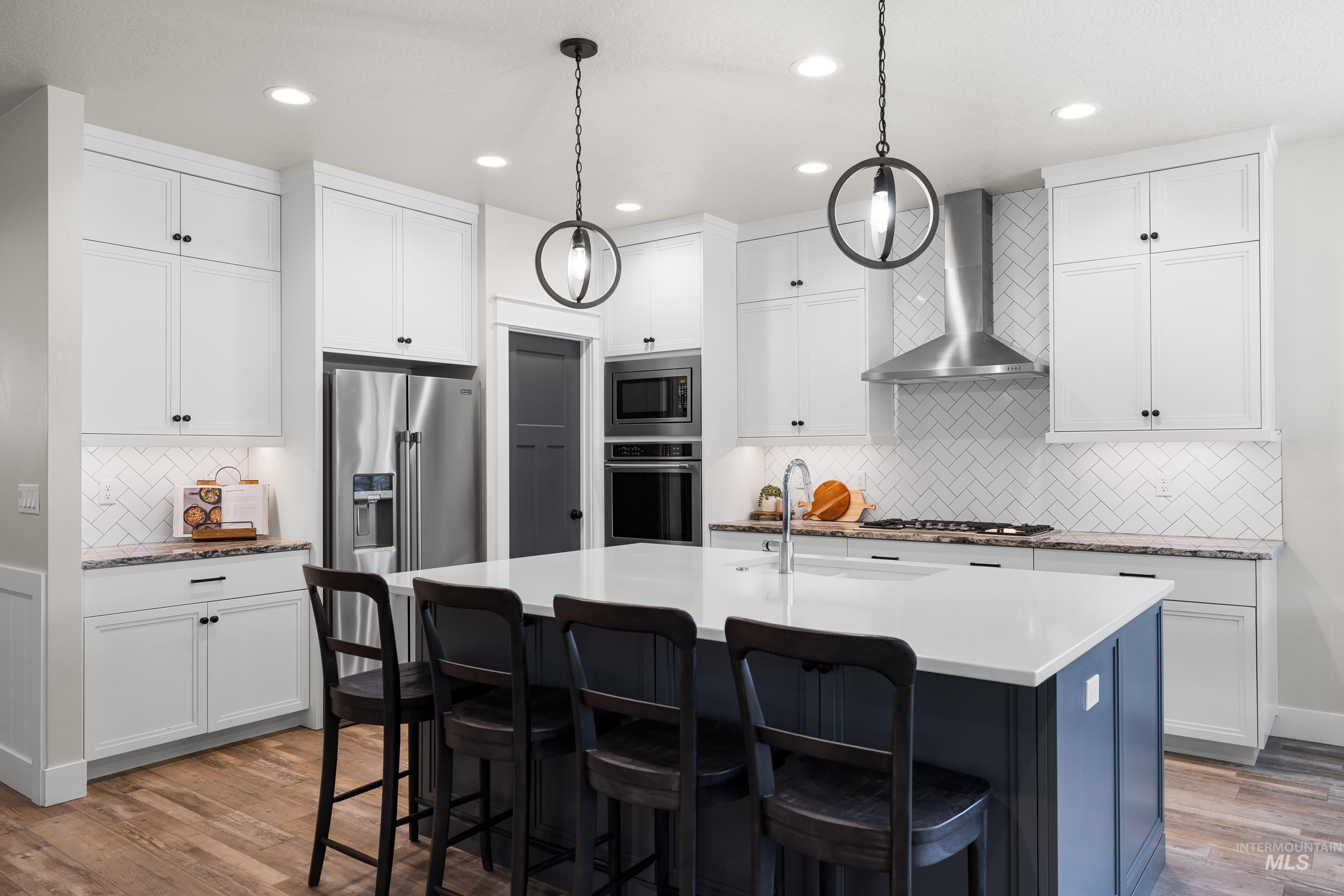 Kitchen featuring wall chimney range hood, stainless steel appliances, tasteful backsplash, wood finished floors, and recessed lighting