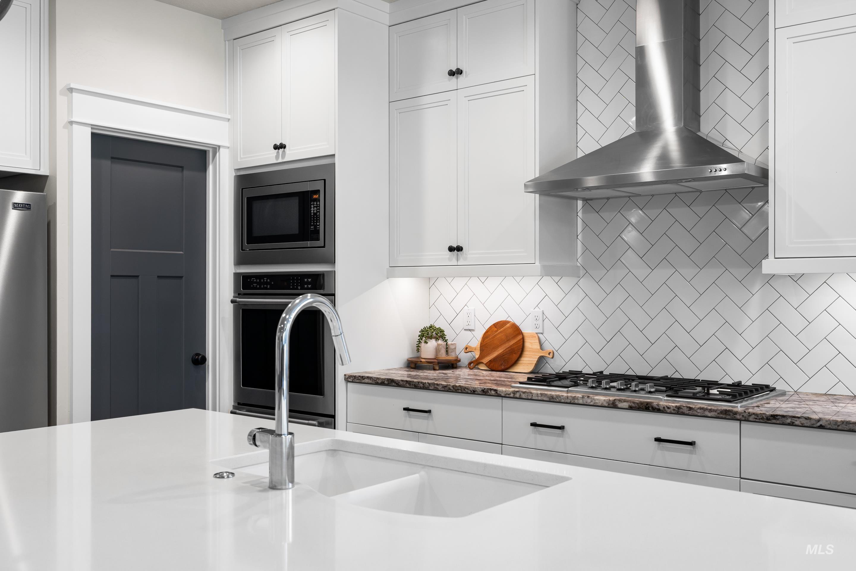 Kitchen with wall chimney range hood, appliances with stainless steel finishes, backsplash, and white cabinetry