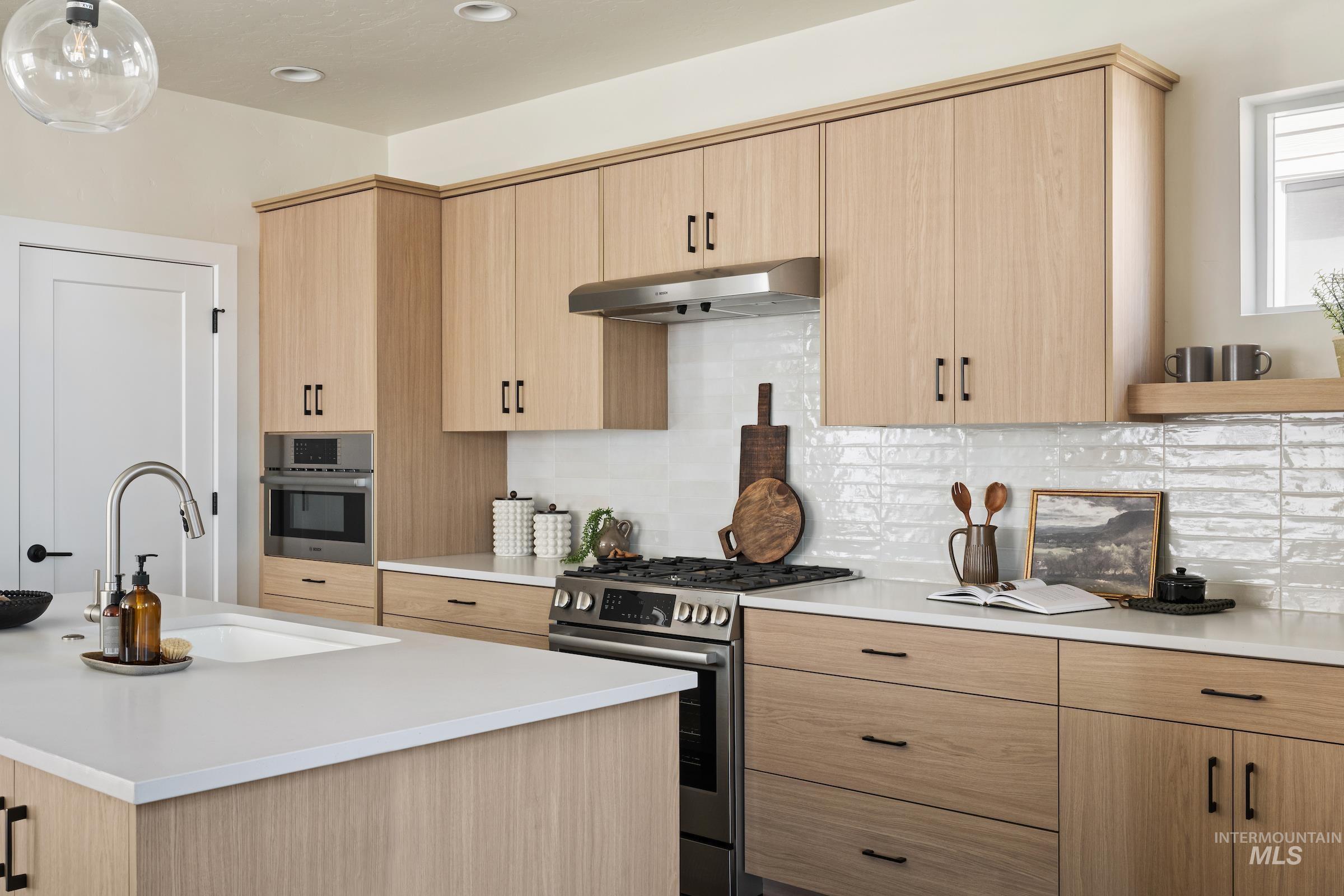 Kitchen featuring light brown cabinets, appliances with stainless steel finishes, tasteful backsplash, and under cabinet range hood