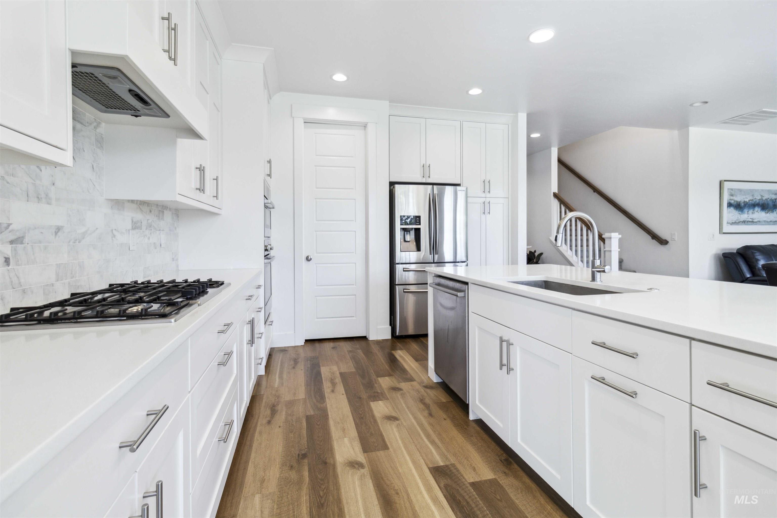 Kitchen with white cabinets, recessed lighting, stainless steel appliances, dark wood-style flooring, and light stone counters