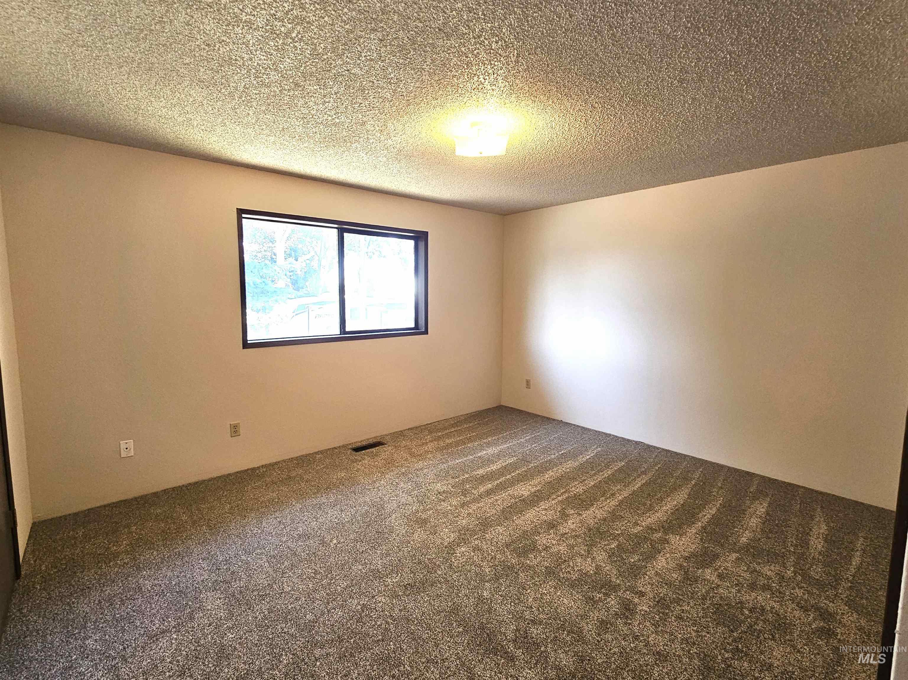 Carpeted spare room with a textured ceiling